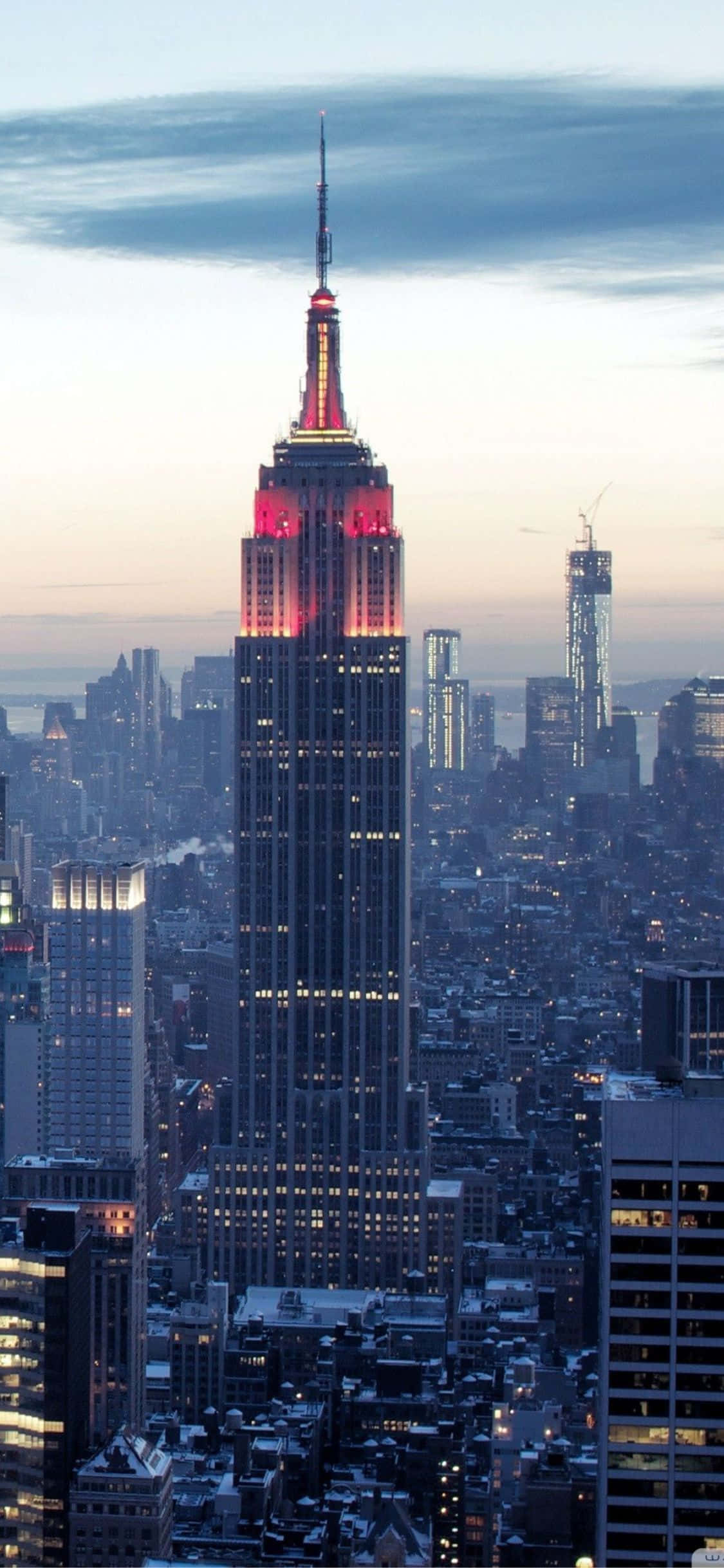 iPhone Xs Ny City 桌布 壁紙 — 帝國大廈在暮色天空下發出紅光，下方密集的城市燈光閃爍。