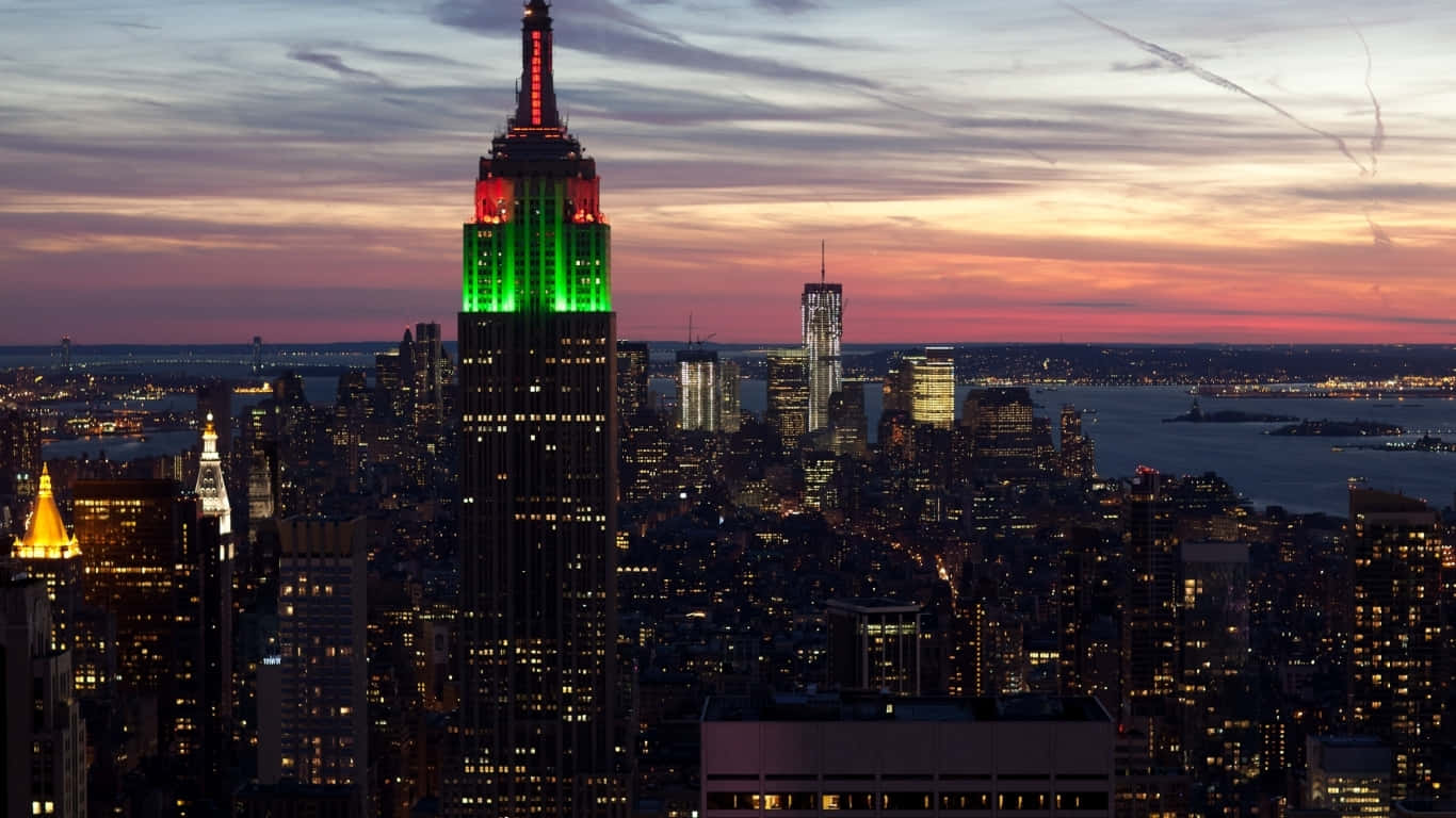 1366x768 Empire State Building 桌布 壁紙 — 帝國大廈在暮色天空下發出綠色光芒，而紐約市的燈光在下方亮起。
