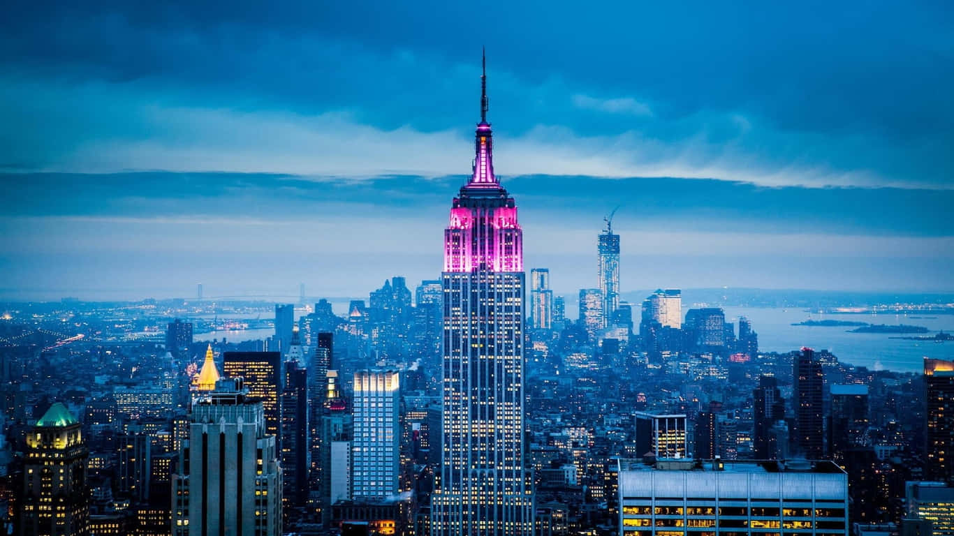 1366x768 Empire State Building 桌布 壁紙 — 帝國大廈在暮色天空中閃耀著粉紅色的光芒，而紐約市的燈光在下方亮起。