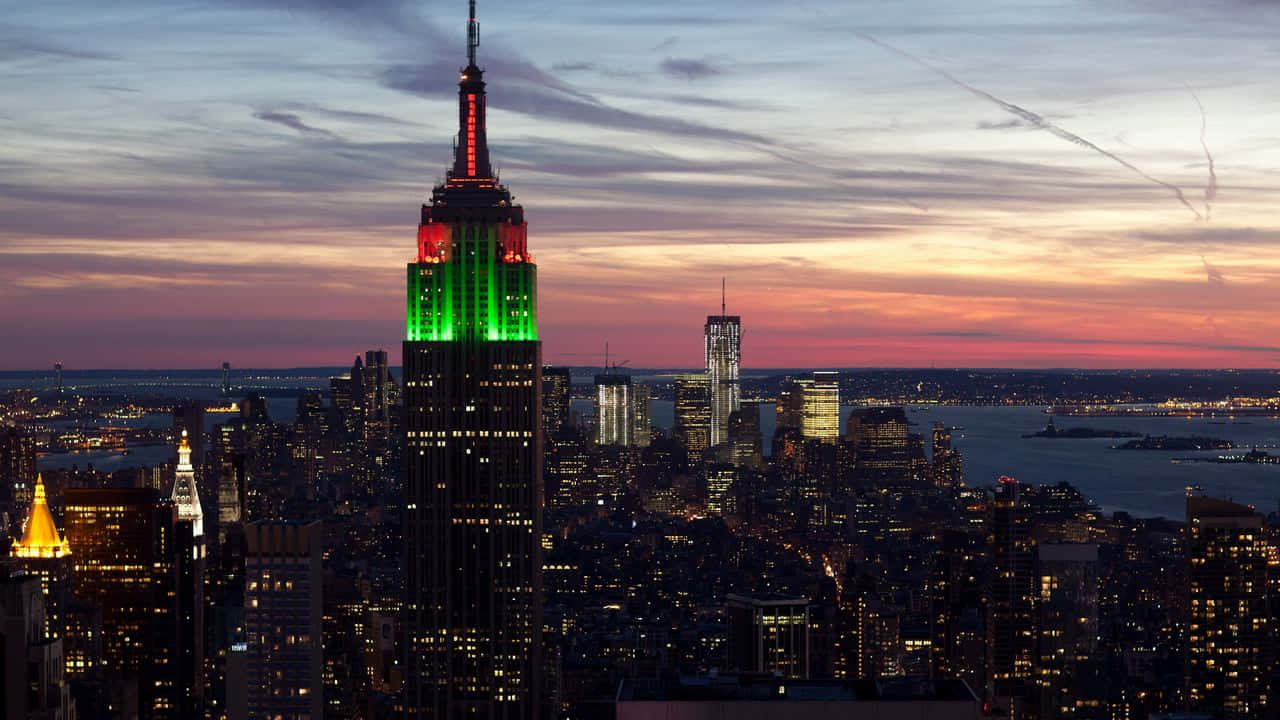 720p Empire State Building 桌布 壁紙 — 帝國大廈在暮色天空中閃耀著綠色光芒，而紐約市的燈光在下方亮起。