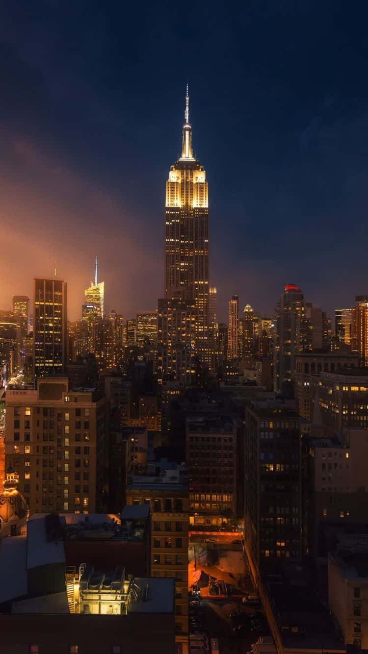 New York City Night iPhone 桌布 壁紙 — 帝國大廈在暮色天空中閃耀金光，下方的紐約天際線被城市燈光照亮。
