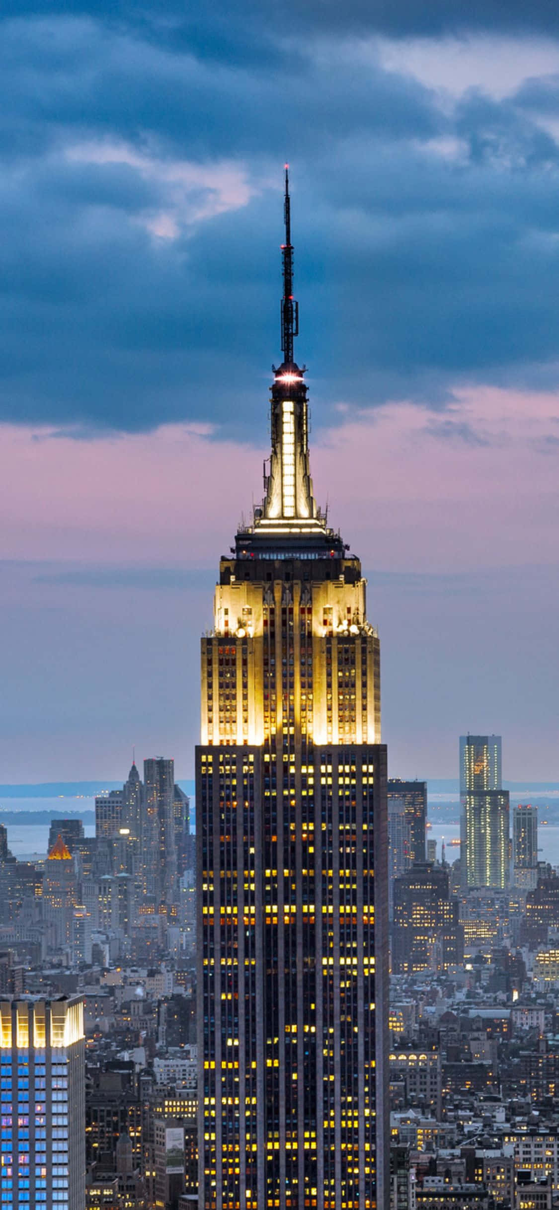iPhone Xs Ny City 桌布 壁紙 — 帝國大廈在暮色天空中閃耀金光，城市燈光在下方閃爍。