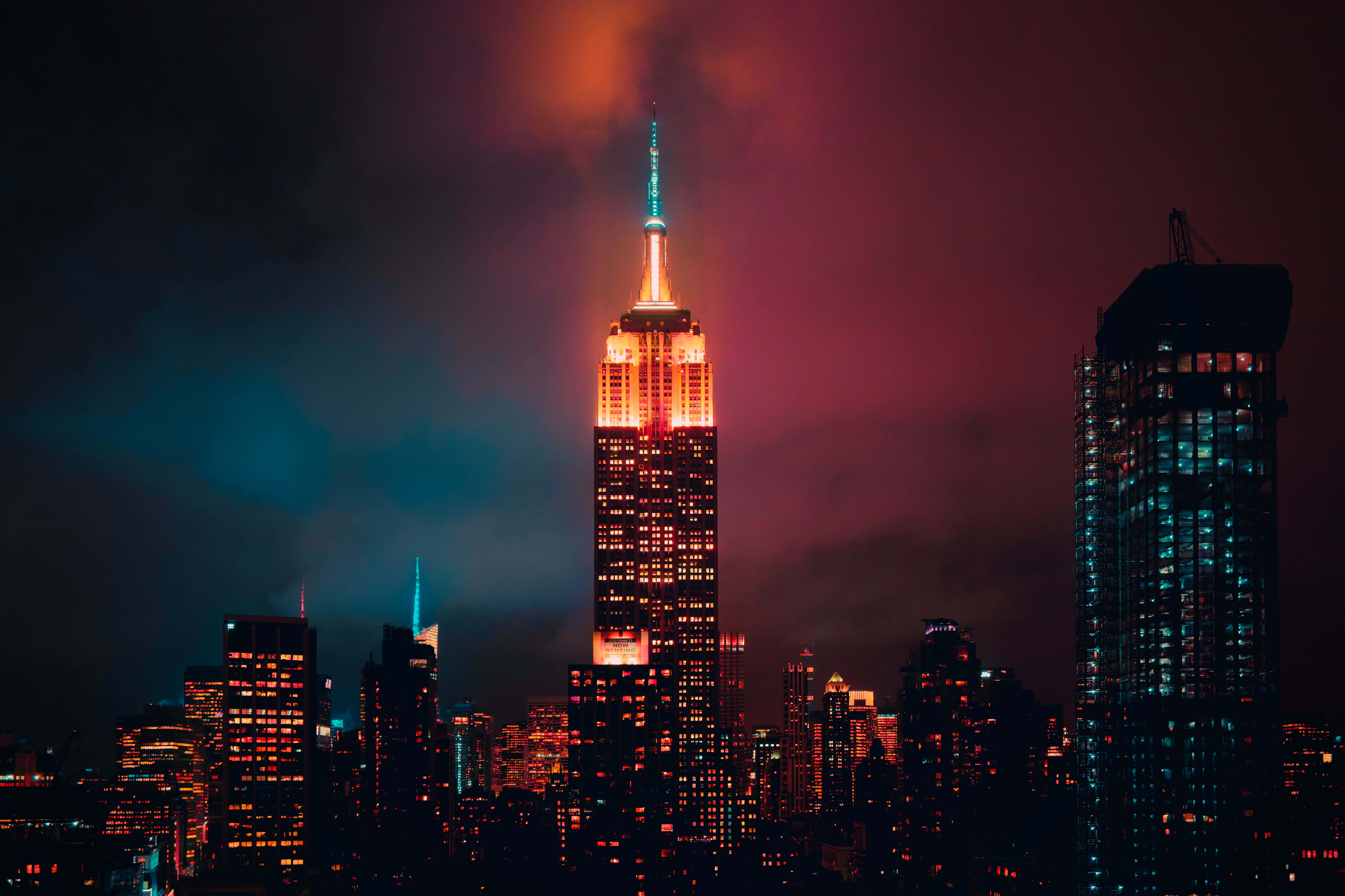 New York State 桌布 壁紙 — 帝國大廈在暮色蒼茫的天空中閃爍著琥珀色和藍綠色，天空中有粉紅色和藍綠色的雲彩。