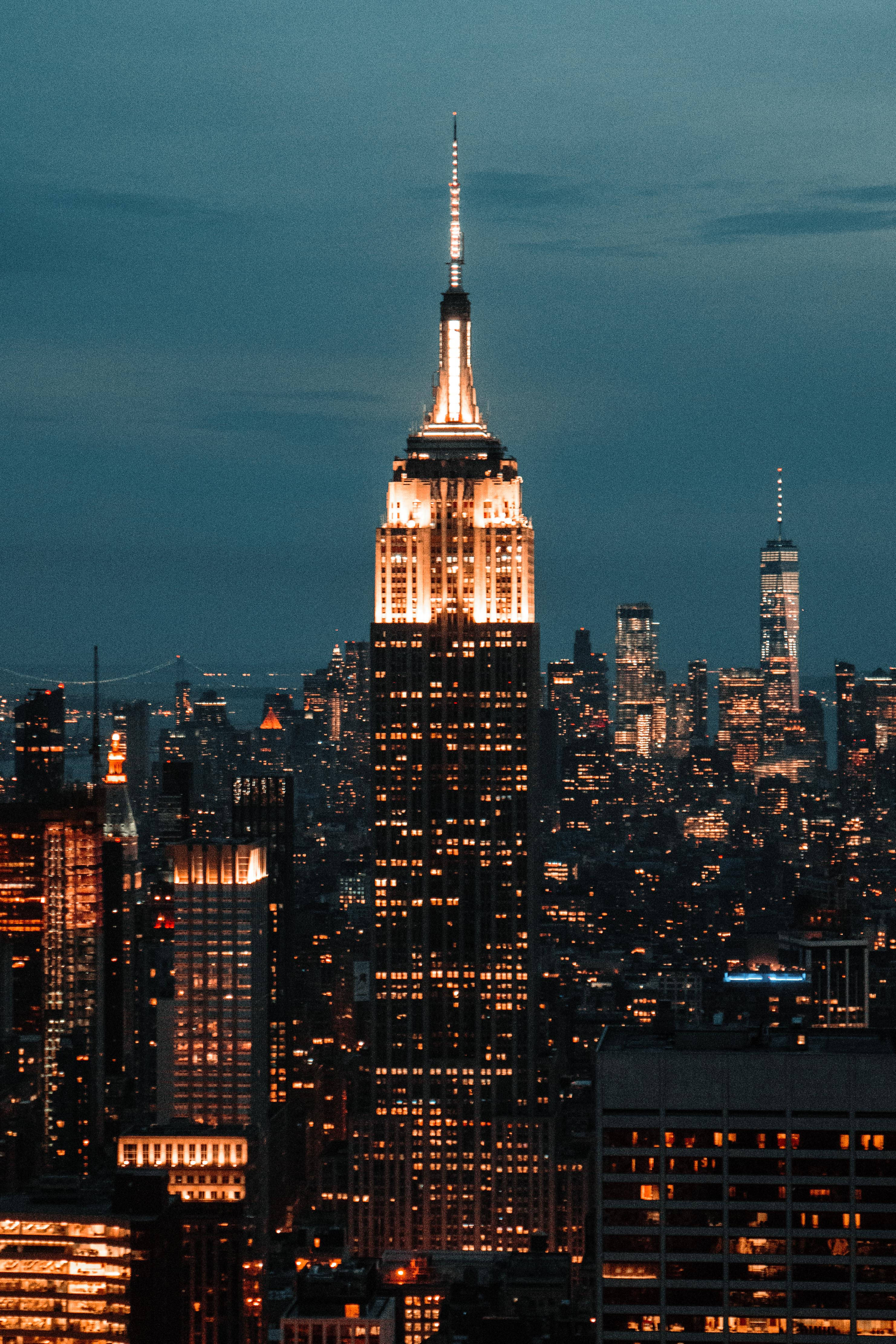empire state 桌布 壁紙 — 帝國大廈在暮色藍天下溫暖地發光，紐約市的天際線在黃昏時分閃爍著城市燈光。