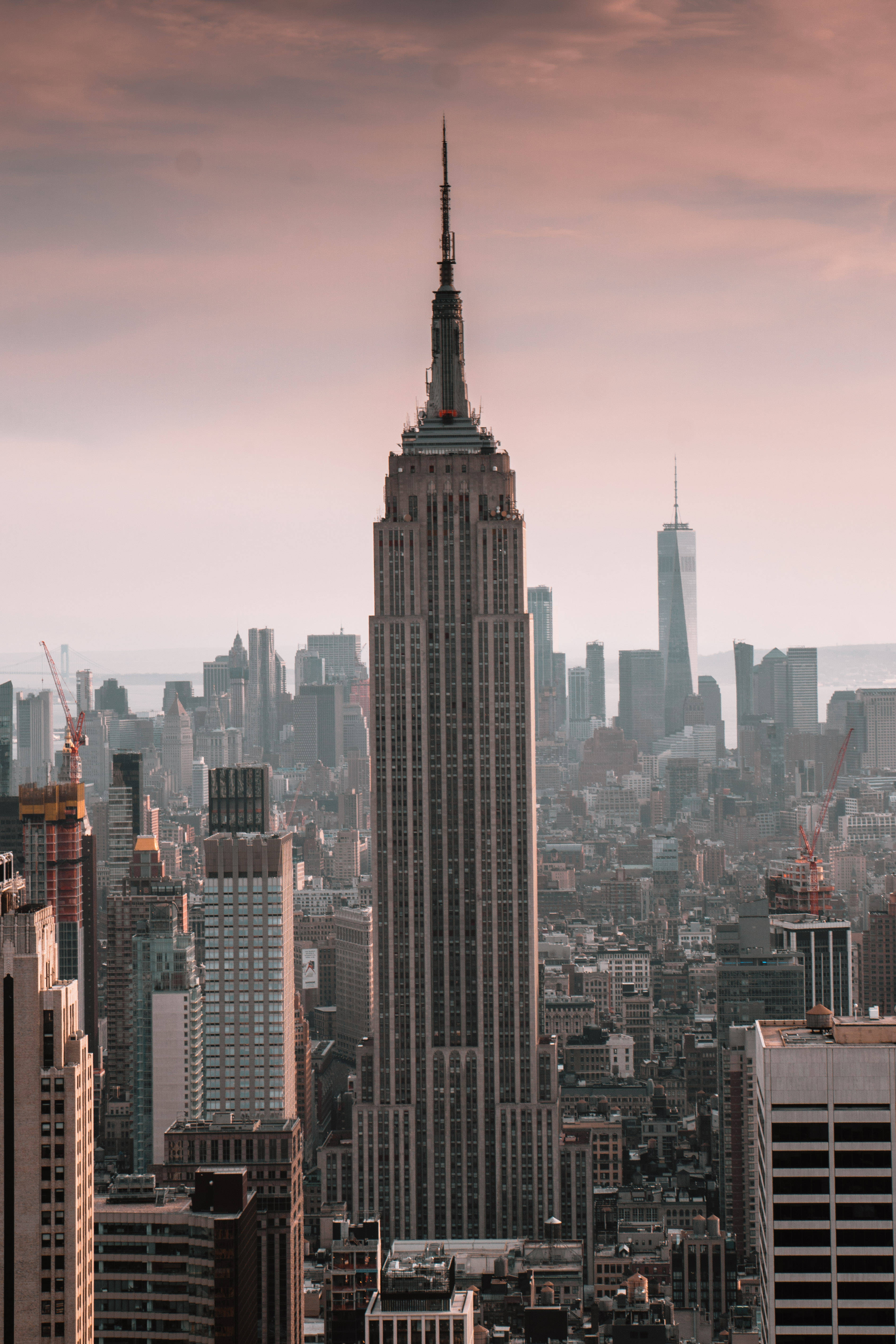 empire state 桌布 壁紙 — 帝國大廈在柔和的粉紅色和橙色暮色天空下，聳立在密集的紐約市天際線之上。