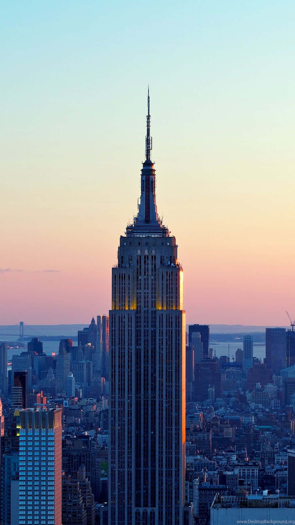 iPhone Xs New York 桌布 壁紙 — 帝國大廈在柔和的粉紅色和藍色日落天空下，聳立在廣闊的紐約市天際線之上。