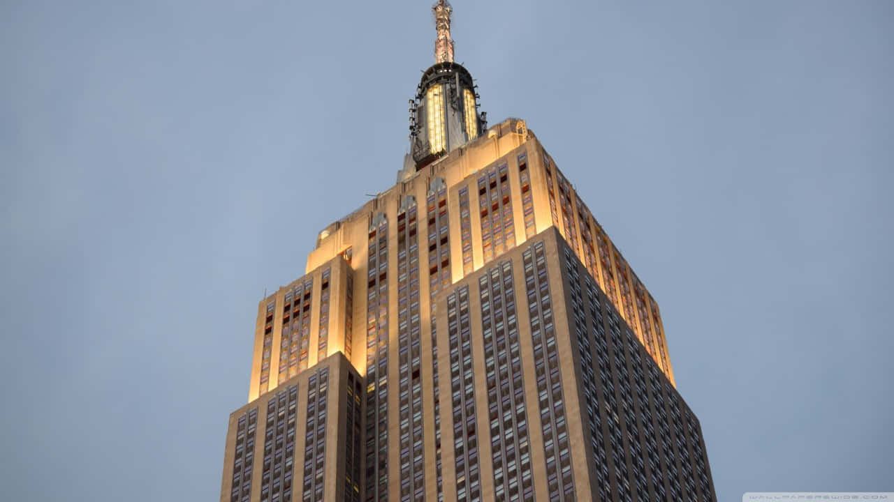 720p Empire State Building 桌布 壁紙 — 帝國大廈在柔和的藍色暮色天空中溫暖地發光，其標誌性的尖頂向上延伸。