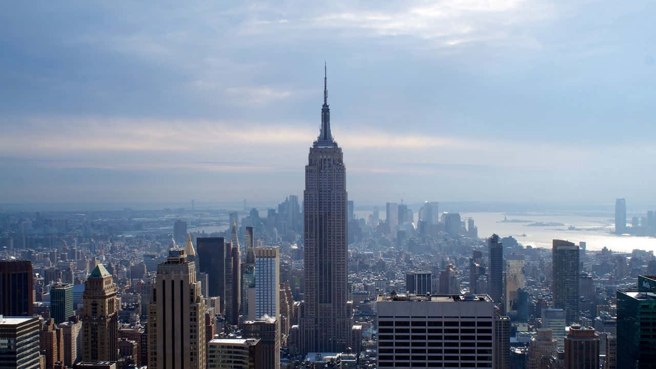 720p Empire State Building 桌布 壁紙 — 帝國大廈在柔和藍天與縷縷白雲下，聳立於廣闊的紐約市天際線之上。