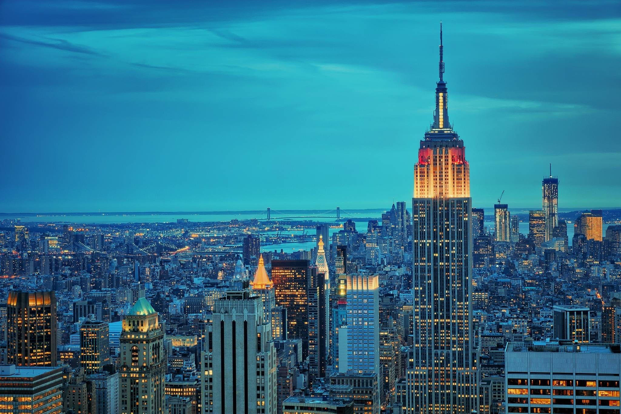 empire state 桌布 壁紙 — 帝國大廈在深藍色的暮色中溫暖地發光，城市的燈光照亮了廣闊的紐約天際線。