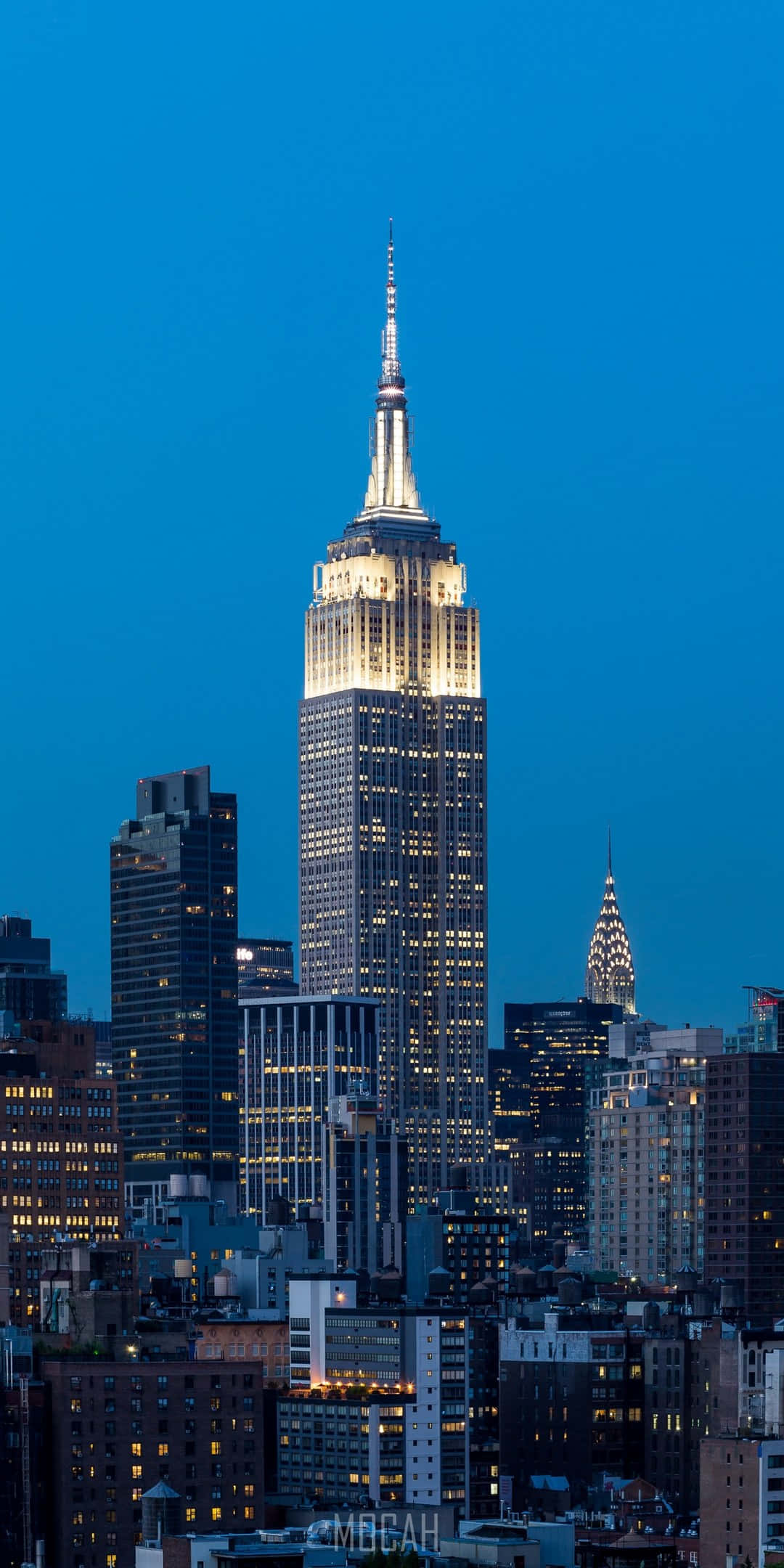 New York State 桌布 壁紙 — 帝國大廈在深藍色的暮色天空中，於密集的紐約市天際線上方溫暖地發光。