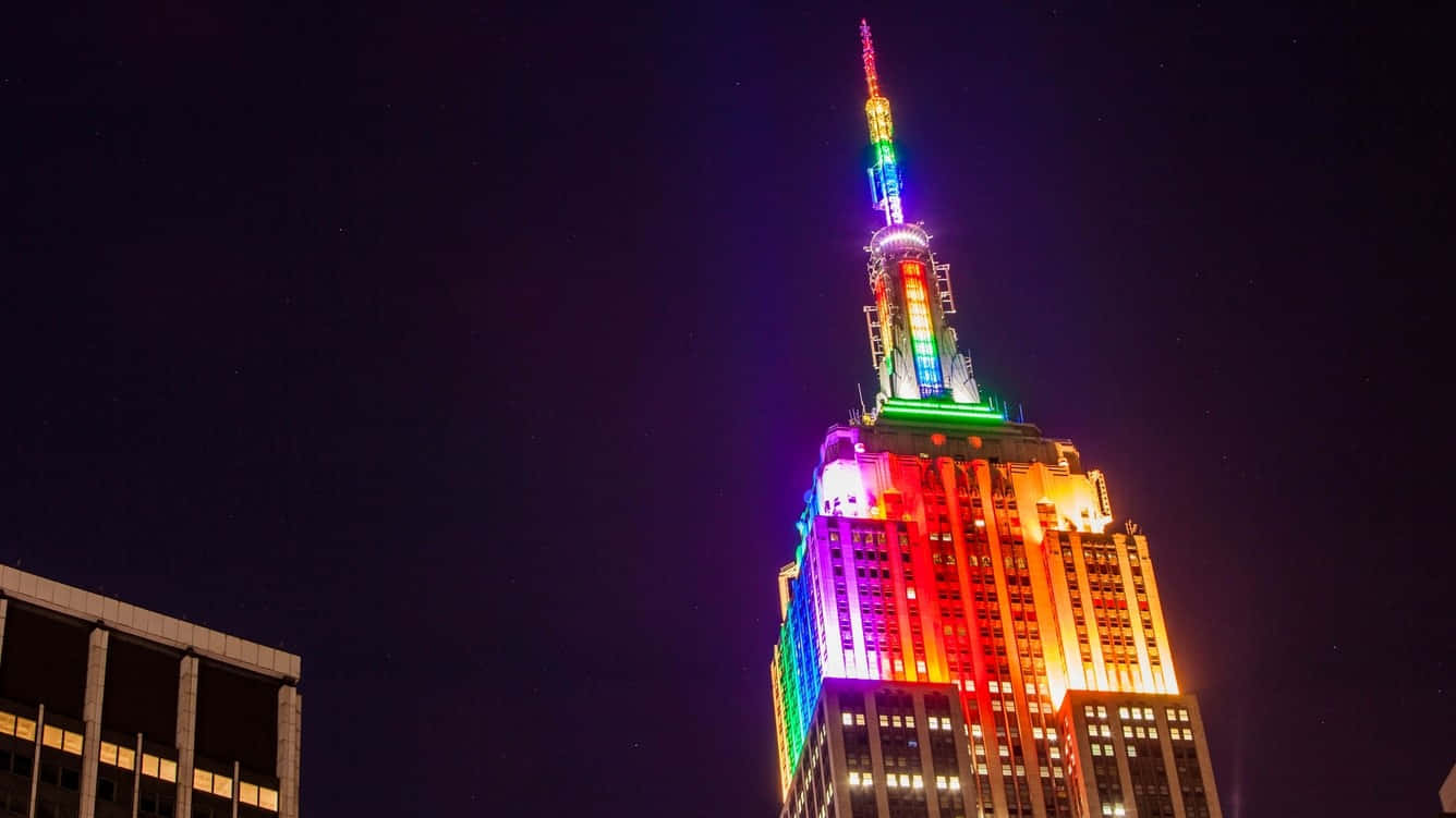 1366x768 Empire State Building 桌布 壁紙 — 帝國大廈在深邃的夜空中閃耀著鮮豔的彩虹燈光，構成迷人的城市夜景。