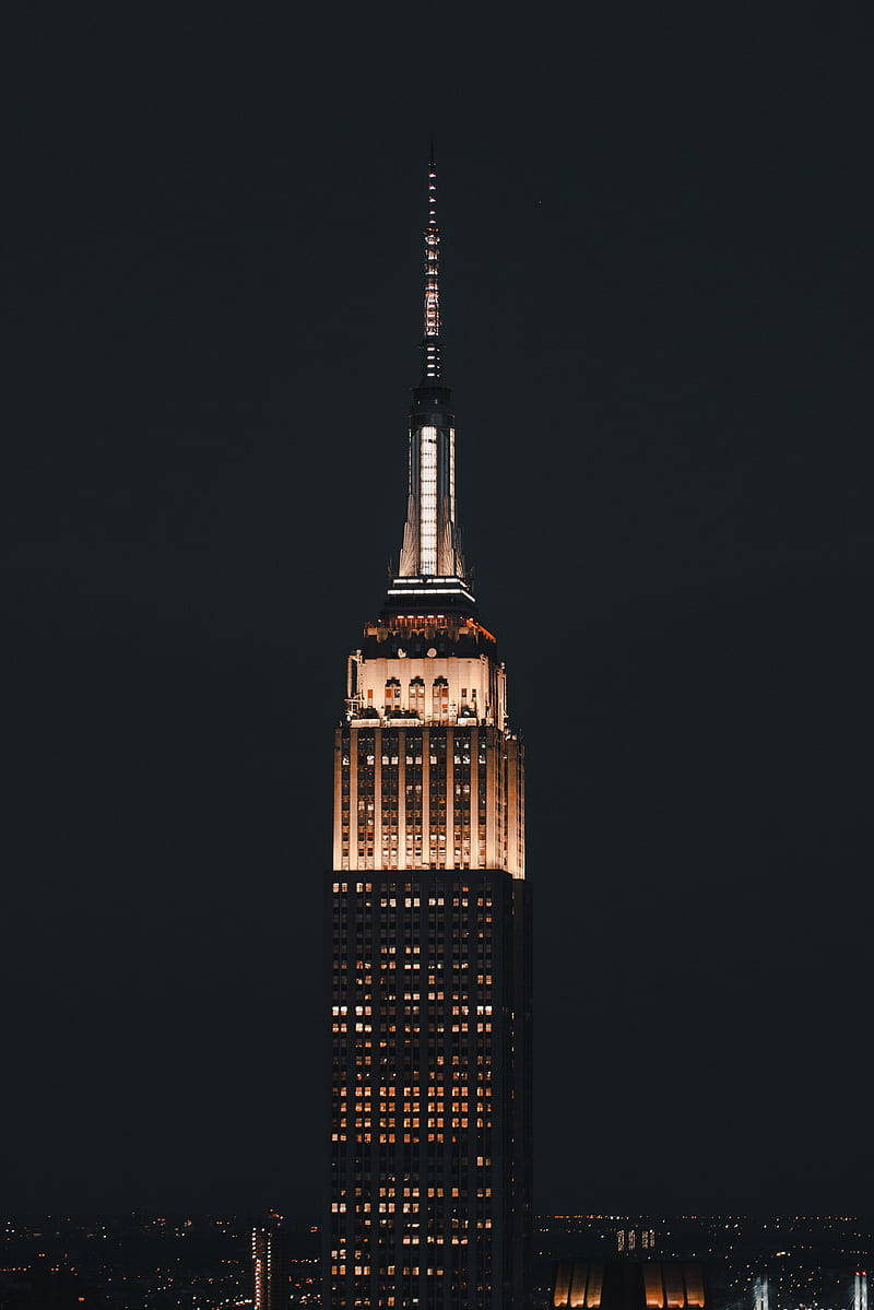 empire 桌布 壁紙 — 帝國大廈在漆黑的夜空中高聳入雲，其標誌性的尖頂和窗戶在城市輪廓中溫暖地閃耀。