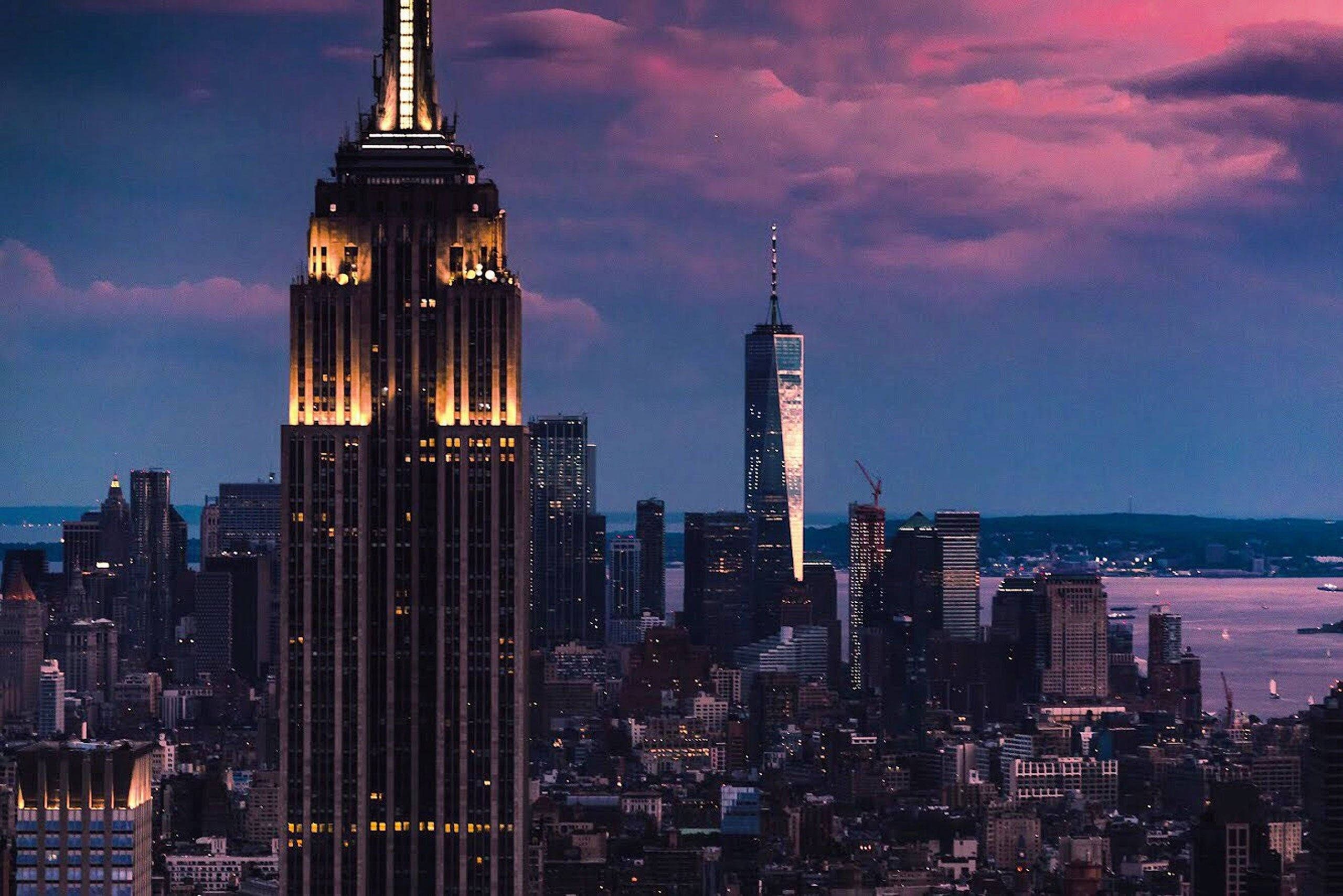 Nyc Aesthetic 桌布 壁紙 — 帝國大廈在紐約市上空帶有粉紅色和紫色雲彩的暮色天空中溫暖地發光。