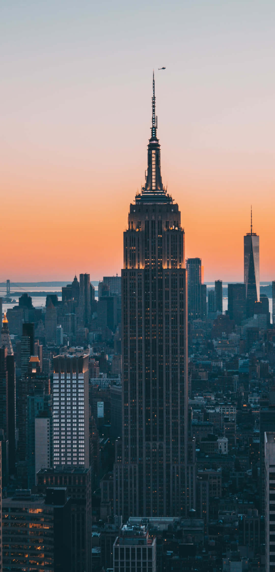 New York State 桌布 壁紙 — 帝國大廈在紐約市廣闊的天際線之上，高聳於充滿活力的橙色日落天空。