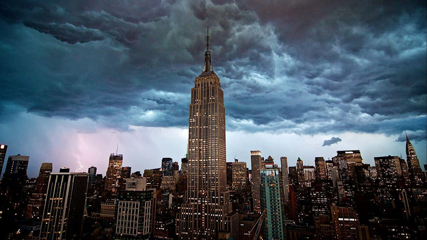 1366x768 Empire State Building 桌布 壁紙 — 帝國大廈在黃昏時分，在閃電劃過紐約市天際線的戲劇性暴風雨天空下亮起。