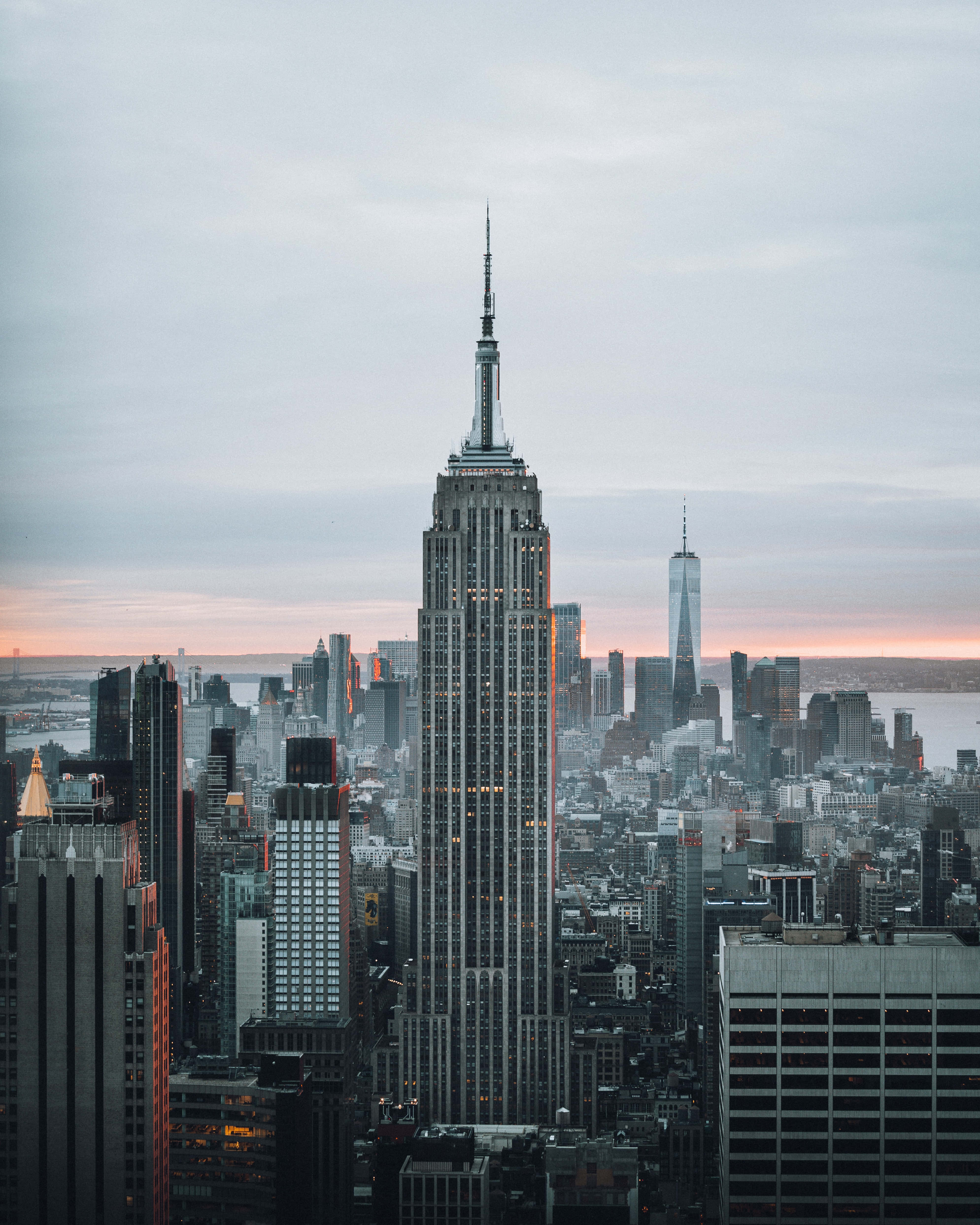 Empire State Building 桌布 壁紙 — 帝國大廈在黃昏時分聳立在密集的紐約市天際線之上，上方有柔和的粉紅色和灰色雲彩。