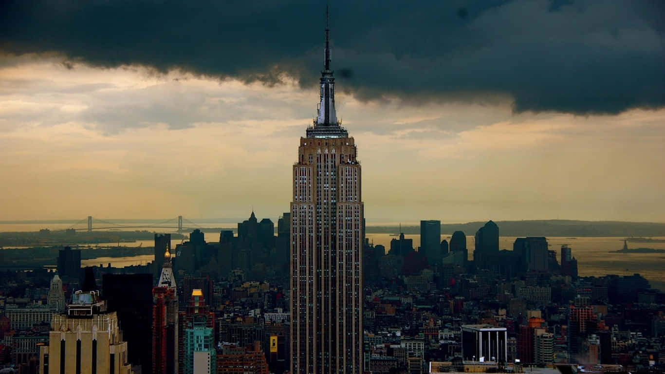 1366x768 Empire State Building 桌布 壁紙 — 帝國大廈在黃昏時分聳立在紐約市上空戲劇性的暴風雨天空下。