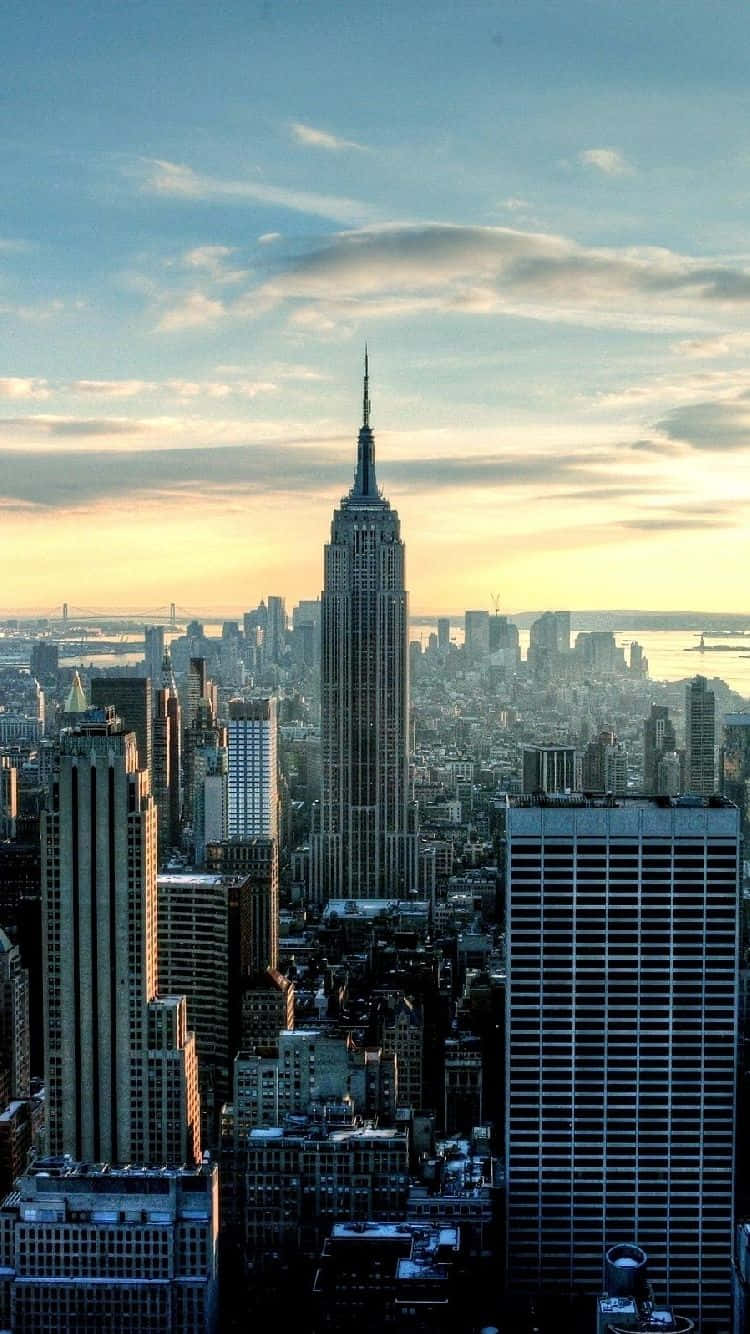 New York 桌布 壁紙 — 帝國大廈在黃金時段聳立在密集的紐約市天際線之上，伴隨著柔和的雲朵和溫暖的光線。