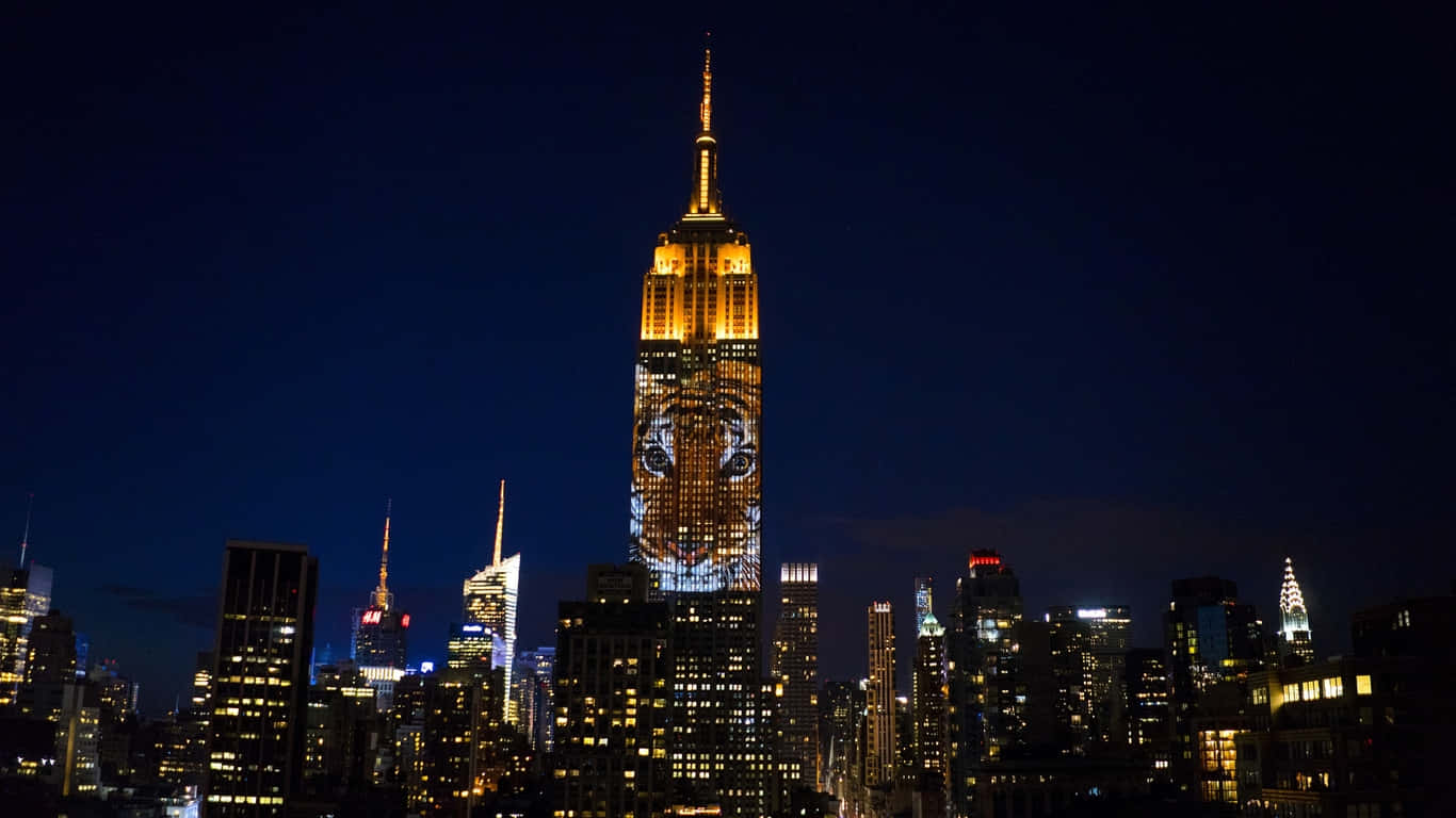 1366x768 Empire State Building 桌布 壁紙 — 帝國大廈在黑暗的夜空下，於燈火通明的紐約市天際線上方，以老虎投影閃耀發光。