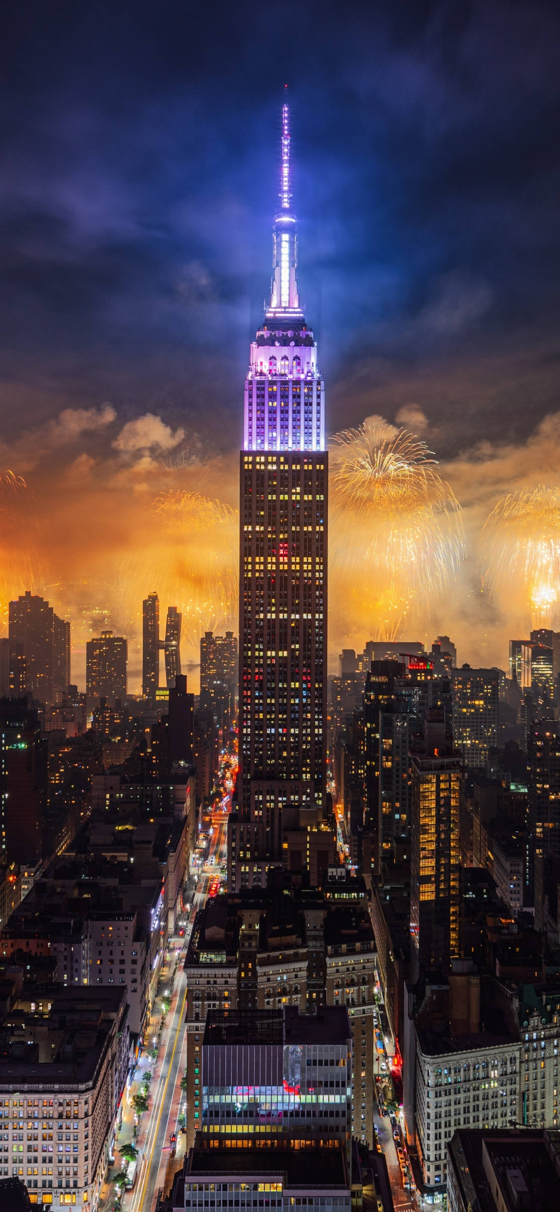 Empire State Building 桌布 壁紙 — 帝國大廈在黑暗的天空中發出紫色光芒，煙火在紐約市上空以金色爆發綻放。