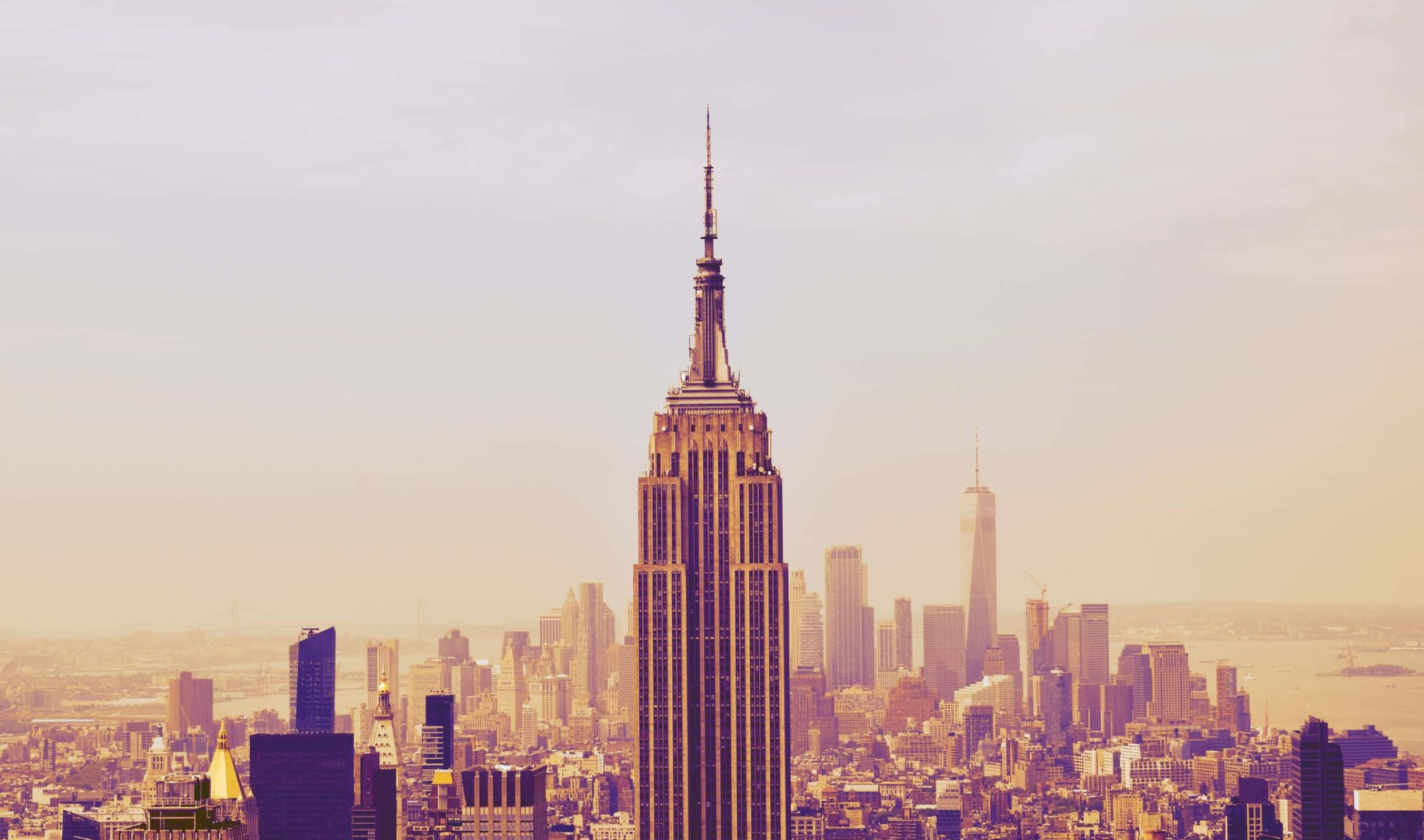 2440x1440 Empire State Building 桌布 壁紙 — 帝國大廈聳立在煙霧瀰漫的紐約天際線上，沐浴在溫暖的金色光芒中。