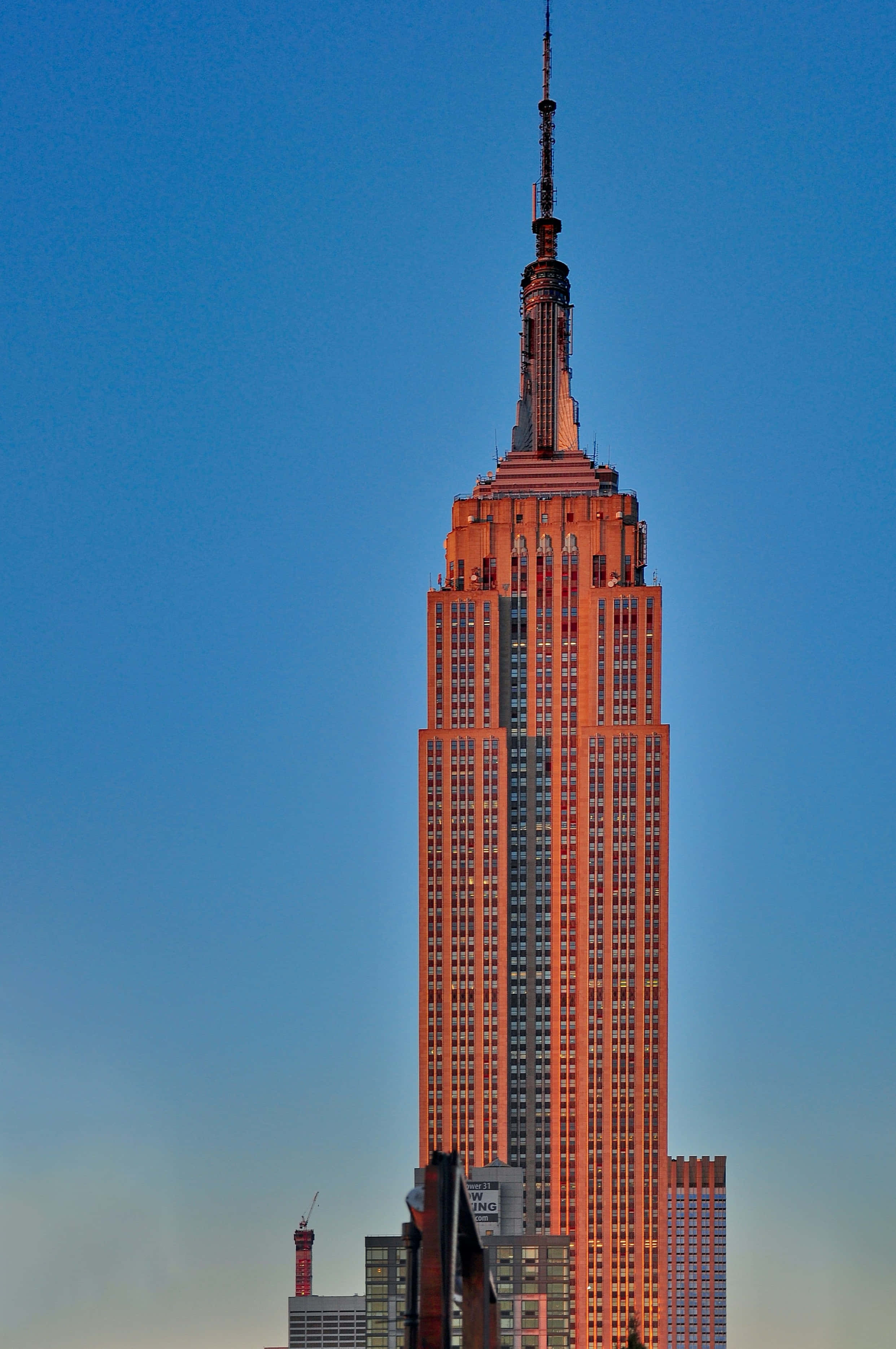 Empire State Building 桌布 壁紙 — 帝國大廈高聳入雲，在清澈的藍天下，溫暖的金色光芒突顯其標誌性的裝飾藝術建築風格。