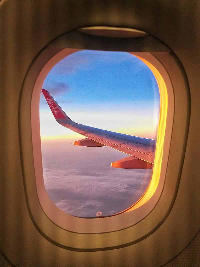 Airplane Window 桌布 壁紙 — 帶有亞洲航空標誌的飛機機翼在透過飛機窗戶看到的日落天空中發光。