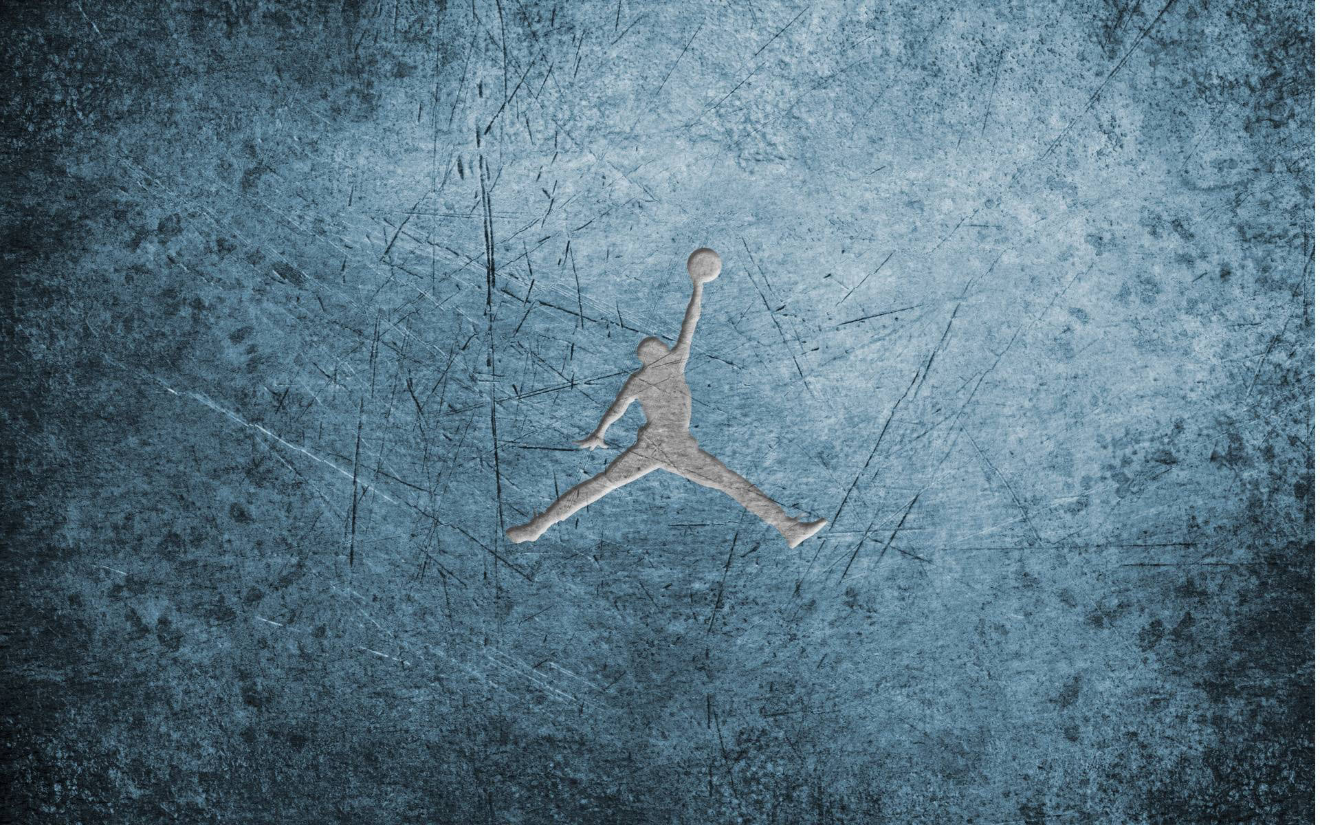 Jordan Logo 桌布 壁紙 — 帶有刮痕的紋理藍色牆壁上，有一個凸起的銀色籃球運動員剪影，在空中持球。