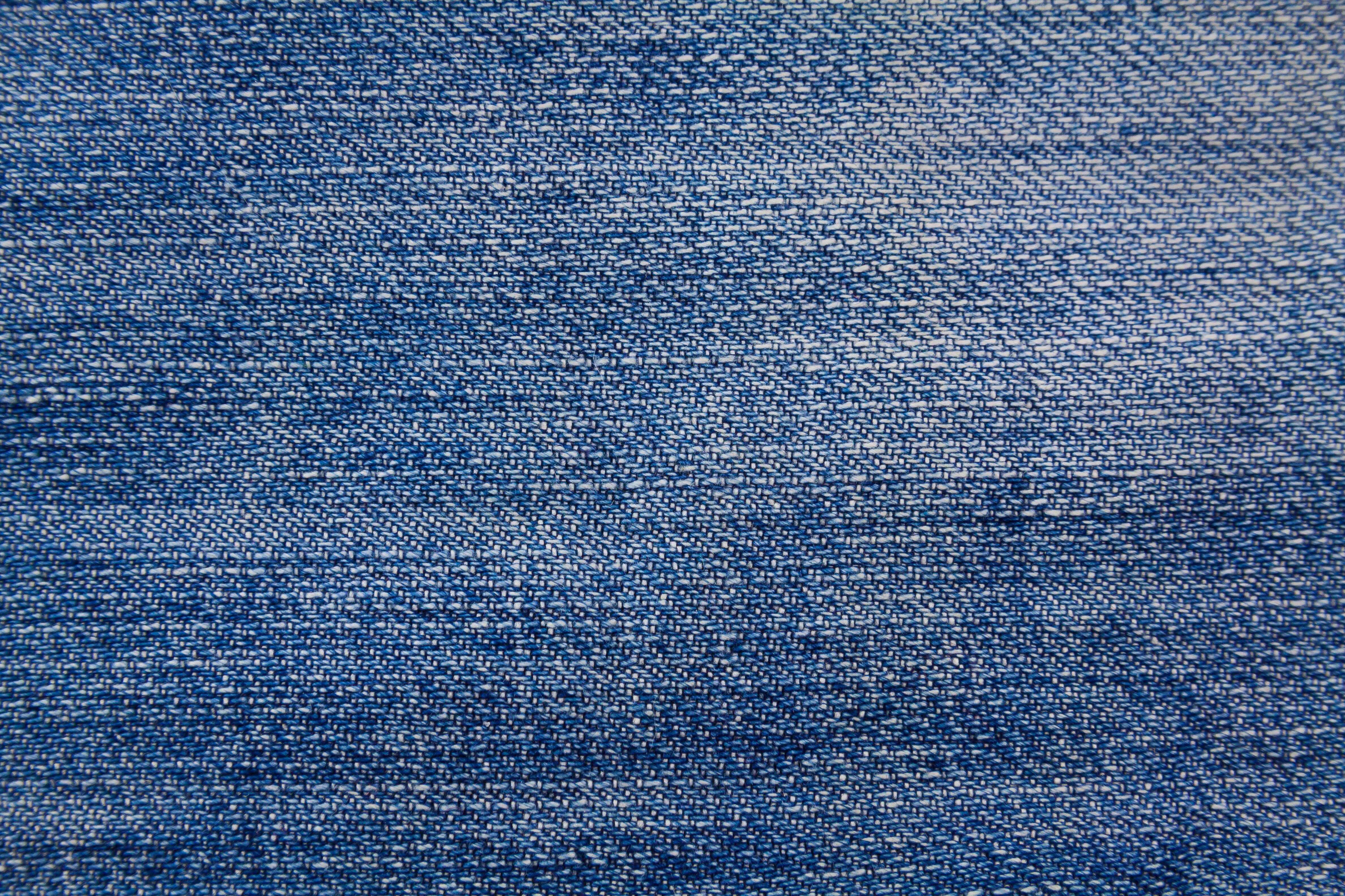 Denim 桌布 壁紙 — 帶有可見編織紋理和細微褪色圖案的藍色牛仔布面料特寫。