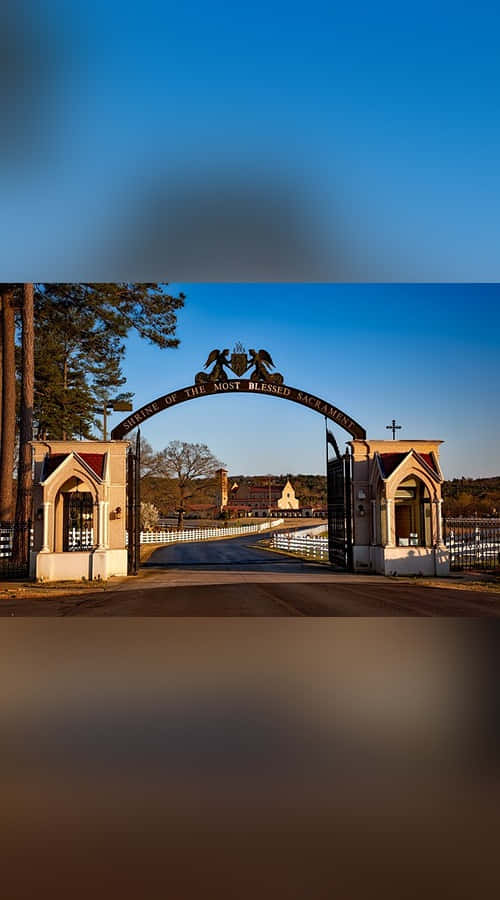 Sacrament 桌布 壁紙 — 帶有宗教標誌的大型拱門矗立在晴朗藍天下寧靜修道院場地的入口處。