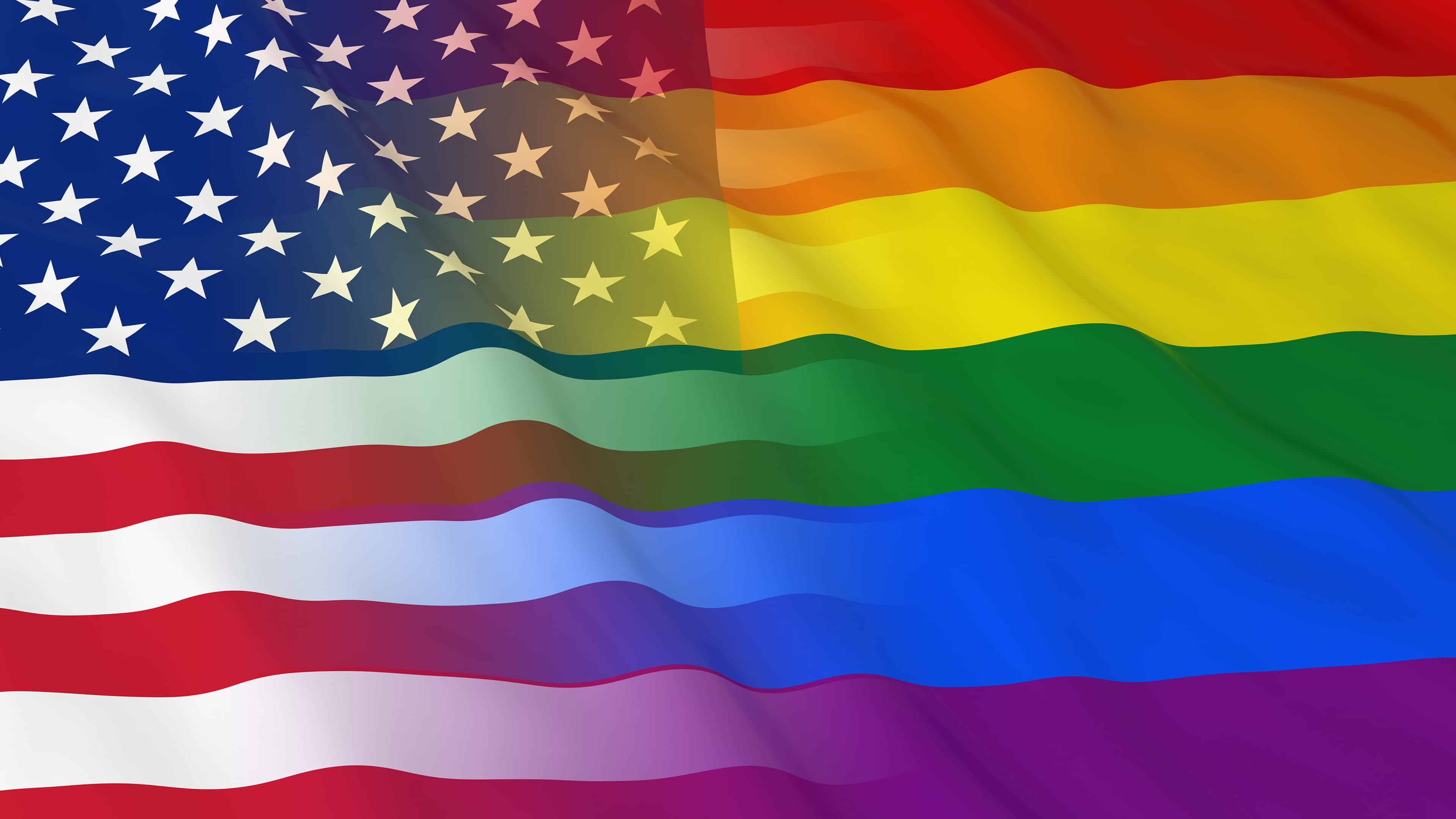 Pride Flag 桌布 壁紙 — 帶有彩虹條紋的美國國旗在晴朗的天空下動態飄揚。