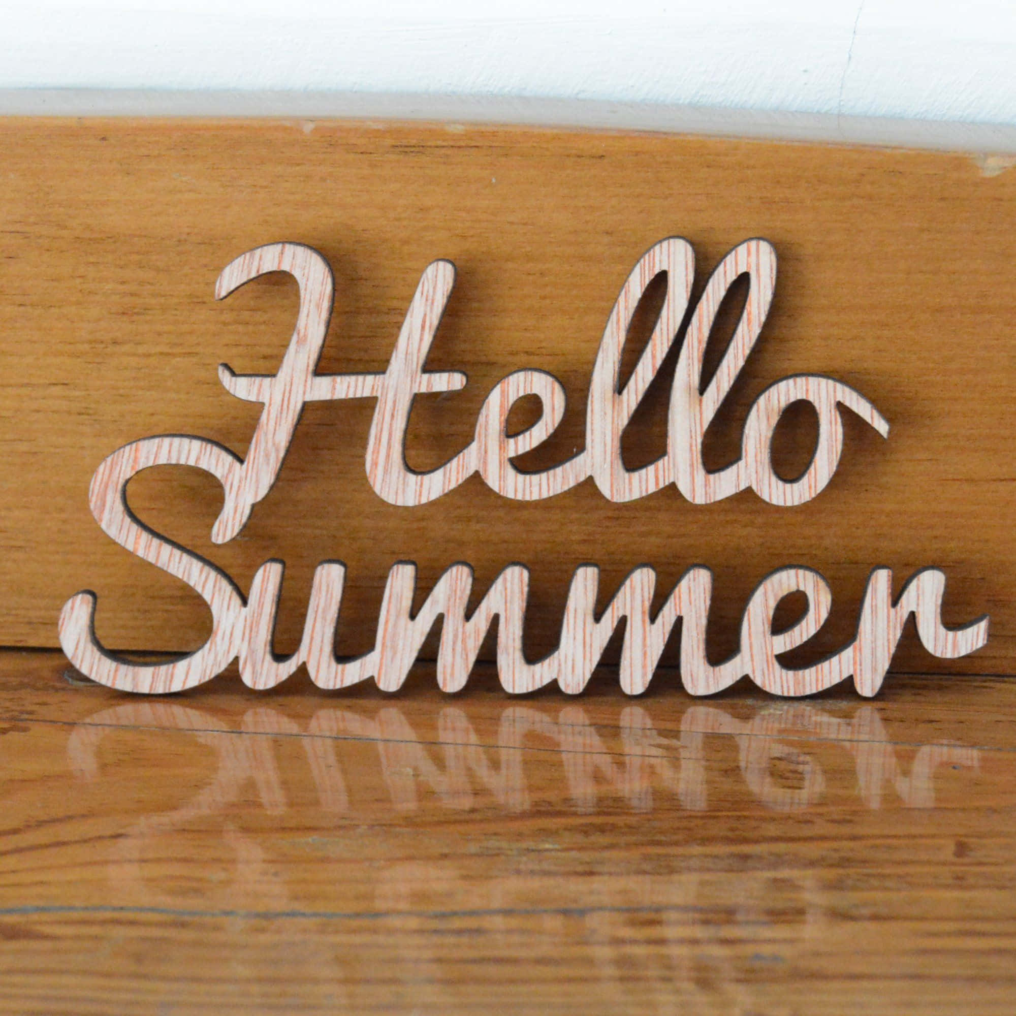 Hello 桌布 壁紙 — 帶有條紋紋理的木製 'Hello Summer' 字母放置在拋光木質表面上，投射出柔和的反光。