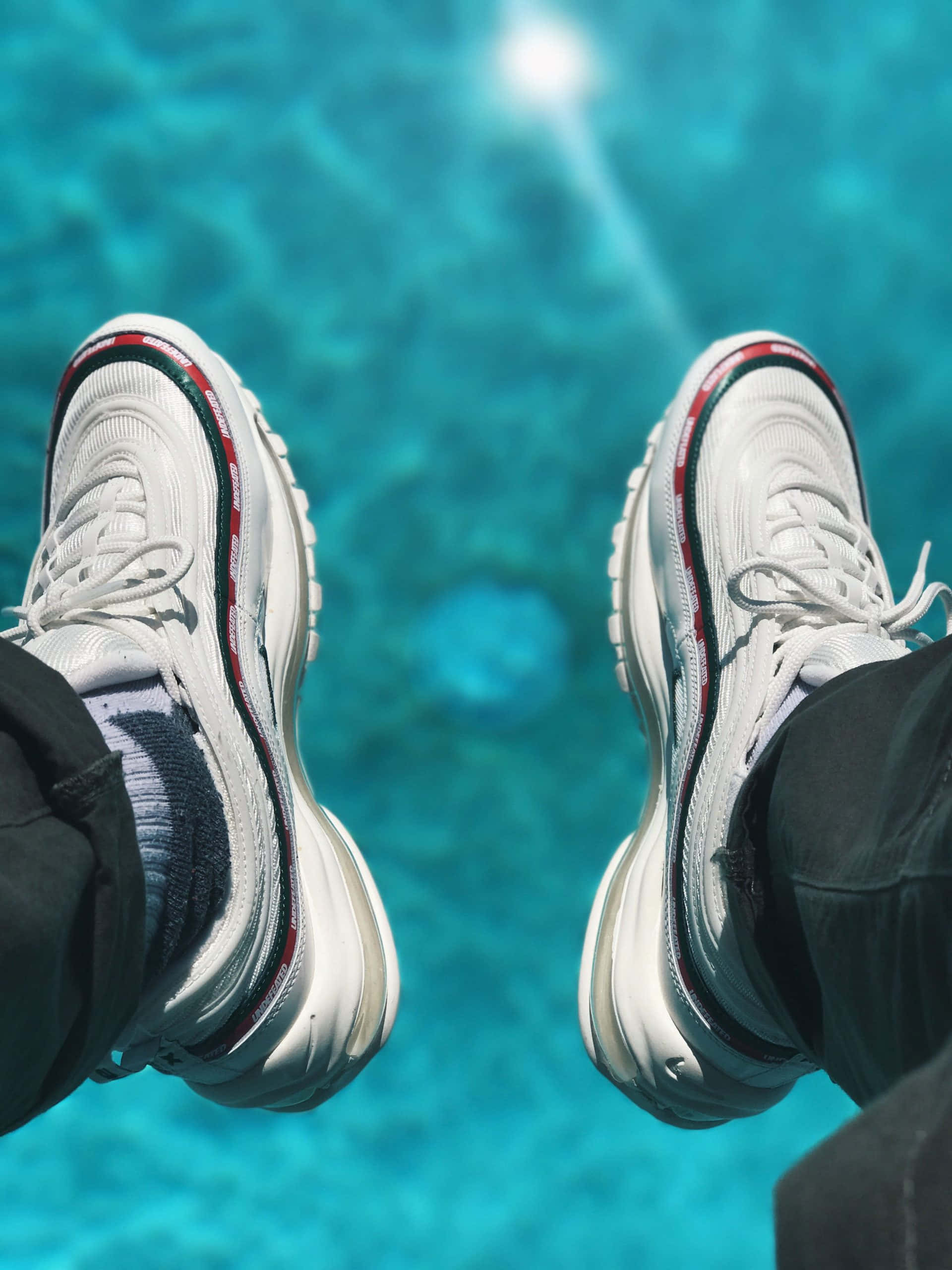 Sneakerhead 桌布 壁紙 — 帶有紅色條紋的白色運動鞋在明亮的陽光下懸掛在清澈的碧藍泳池水面上方。