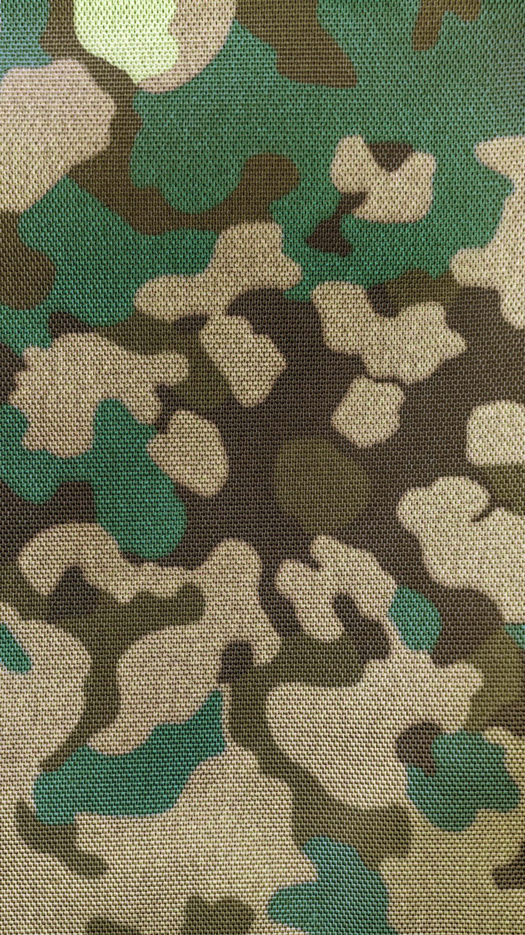 軍事動圖 桌布 壁紙 — 帶有綠色、棕色和米色斑點的紋理軍用迷彩布料的特寫。