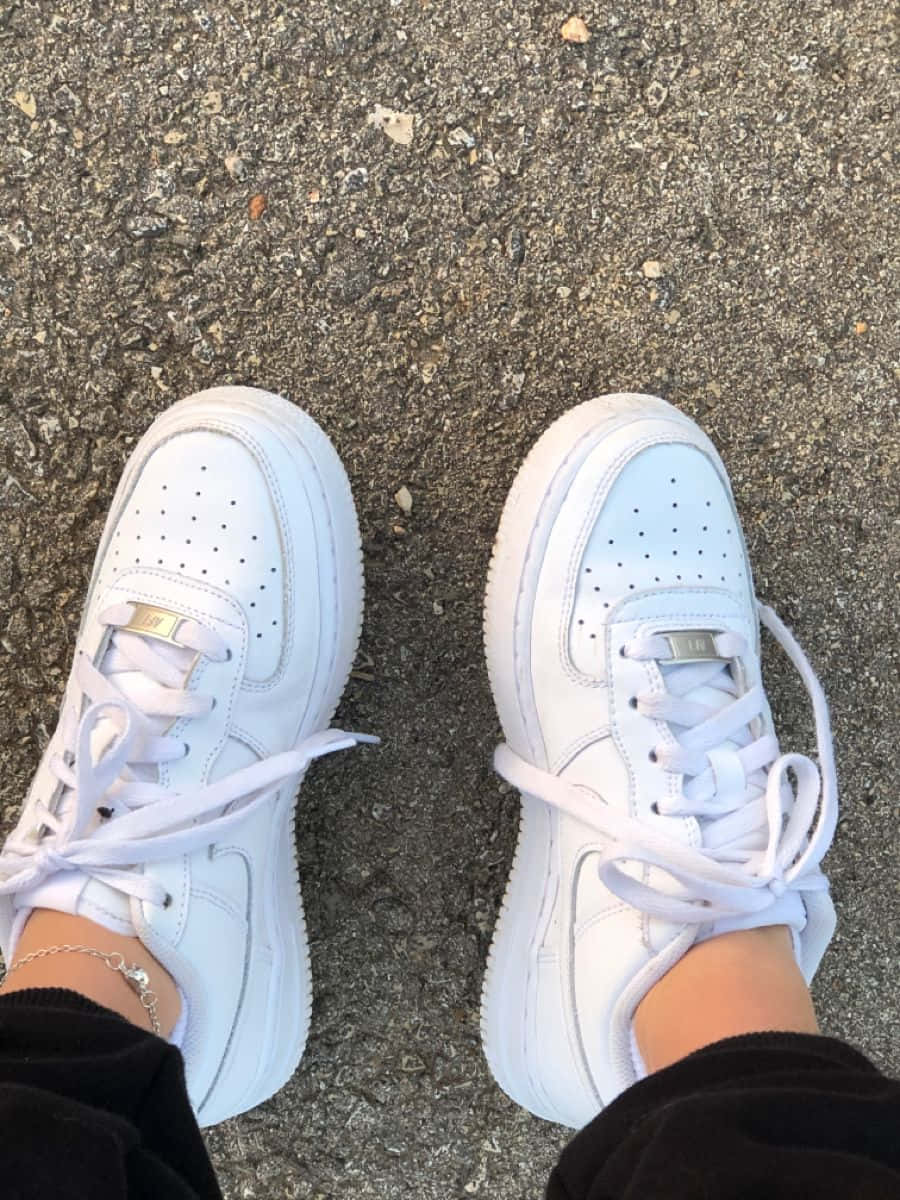 Nike Air Force 桌布 壁紙 — 帶有金色點綴的白色運動鞋從俯視角度放置在質感瀝青路面上。