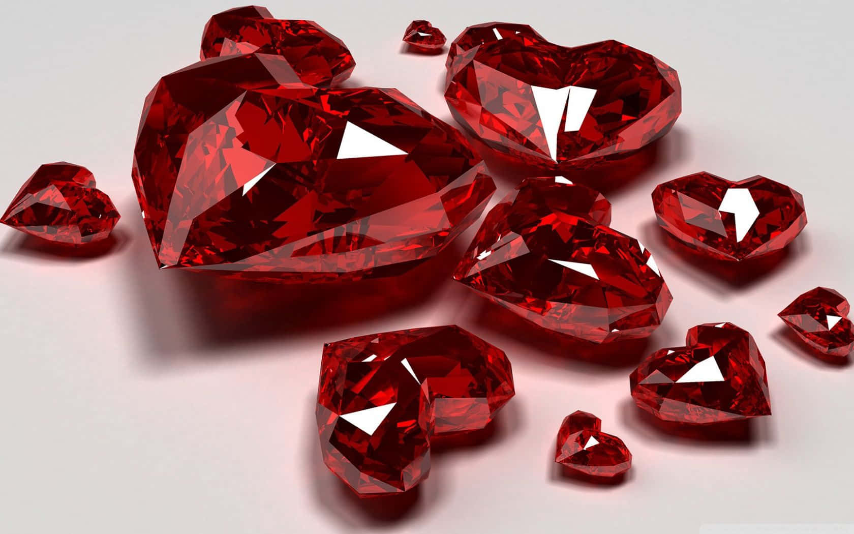 Red Diamond 桌布 壁紙 — 帶有銳利切面和明亮白色高光的亮面紅色心形寶石，放置在純淺灰色表面上。