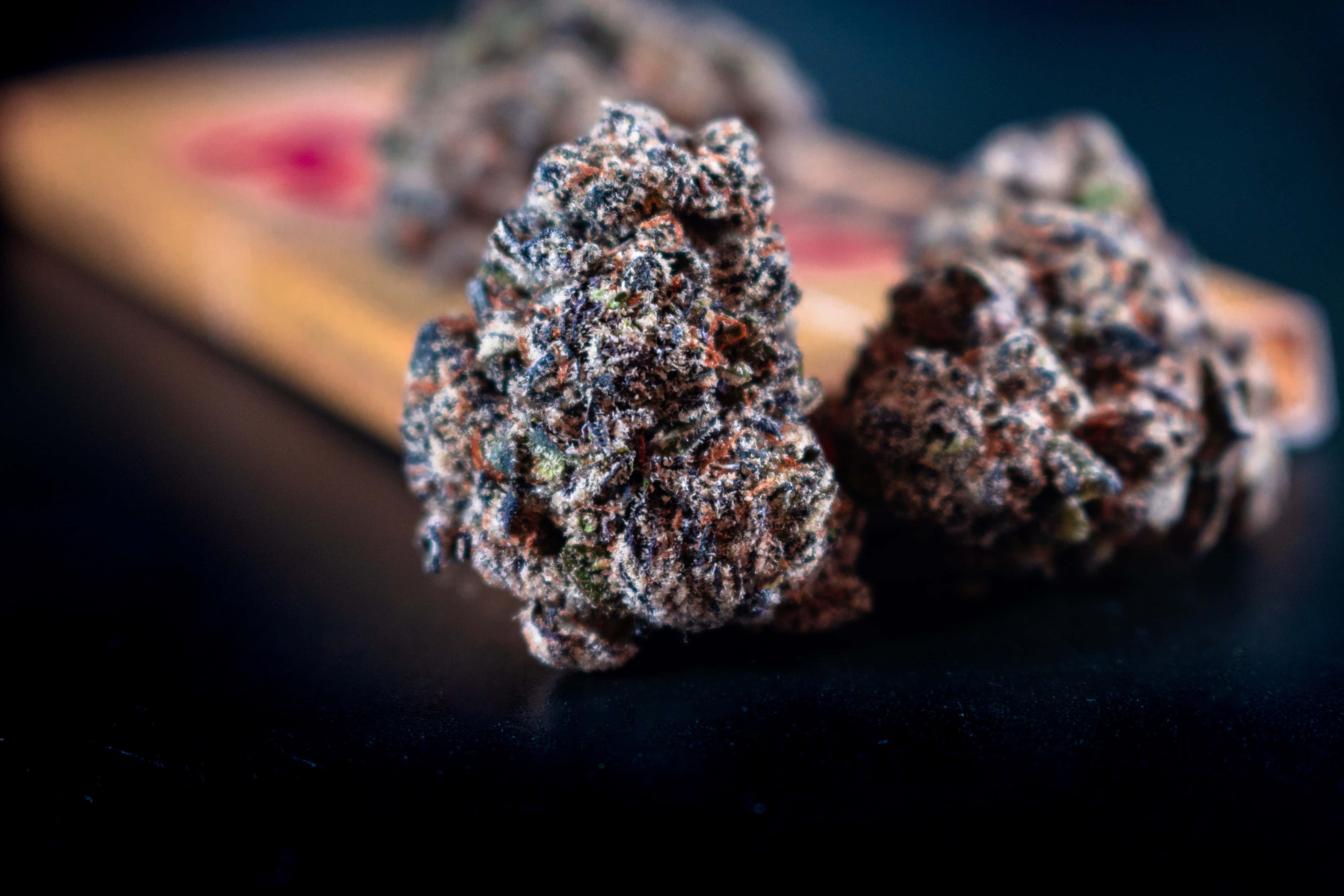 Weed Blunt 桌布 壁紙 — 帶有霜狀毛狀體的紋理大麻花蕾特寫，放置在深色表面上，背景為模糊的木質。