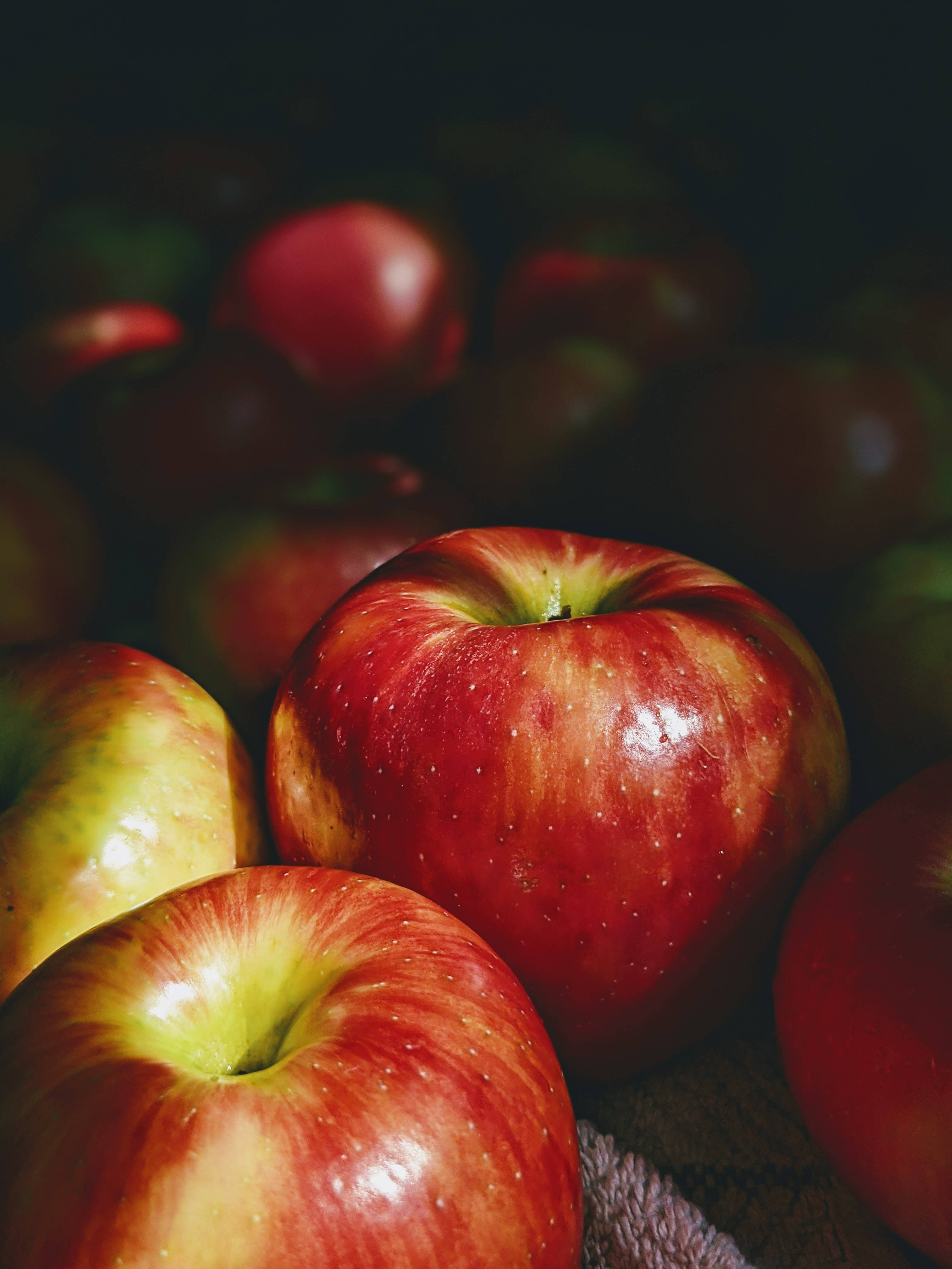 Fruit 桌布 壁紙 — 帶有黃色底色的光澤紅蘋果在柔焦中置於深色背景前，突顯其新鮮質地和自然瑕疵。
