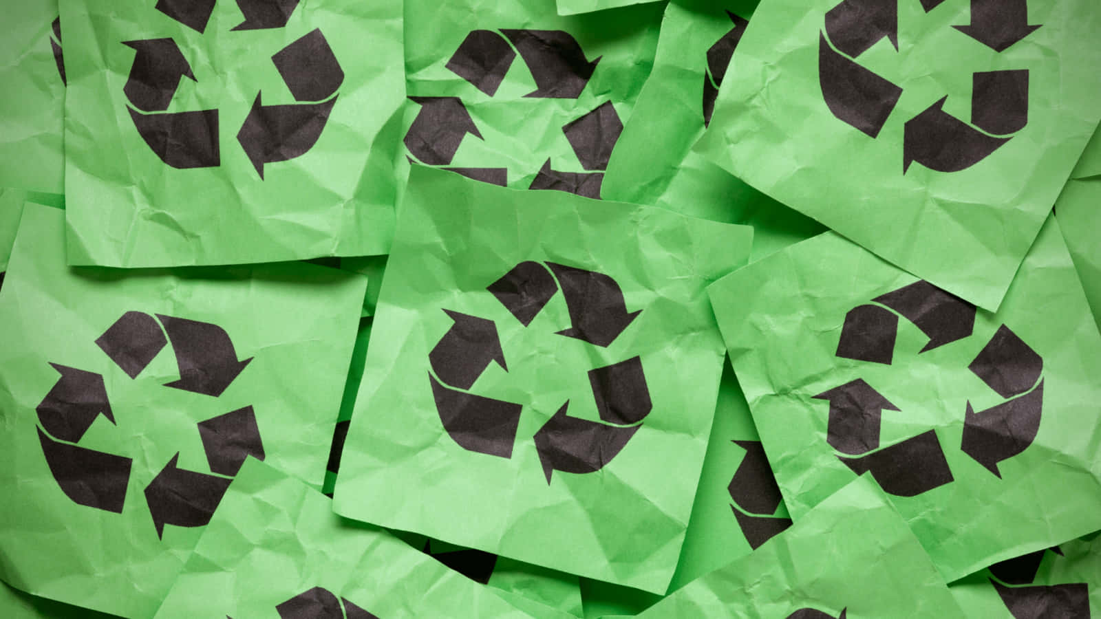 Recycling 桌布 壁紙 — 帶有黑色回收標誌的皺綠色紙張方塊，散落在有紋理的圖案中。