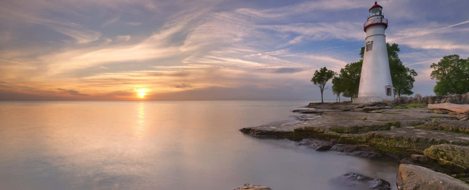 Lake Erie 桌布 壁紙 — 平靜水域上寧靜的日落，白色燈塔矗立在岩石海岸，天空柔和金黃。