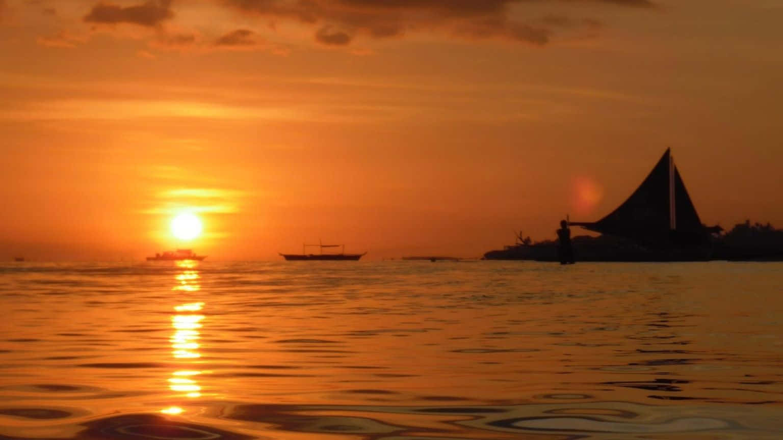 1536x864 桌布 壁紙 — 平靜水面上寧靜的日落，船隻剪影和傳統帆船映襯著火紅的橙色天空。
