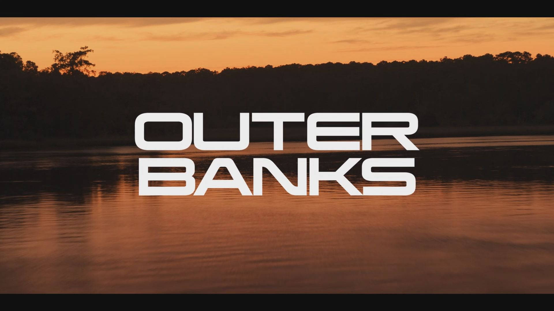 Banks 桌布 壁紙 — 平靜水面上的日落，粗體白色「OUTER BANKS」文字疊加在剪影樹木上。