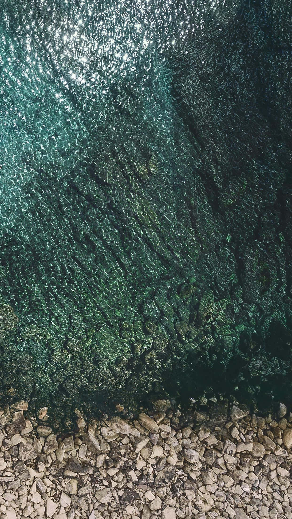 iPad Pro 桌布 壁紙 — 平靜海岸線上，清澈碧綠的海水在陽光照射的岩石上泛起漣漪的航拍視圖。