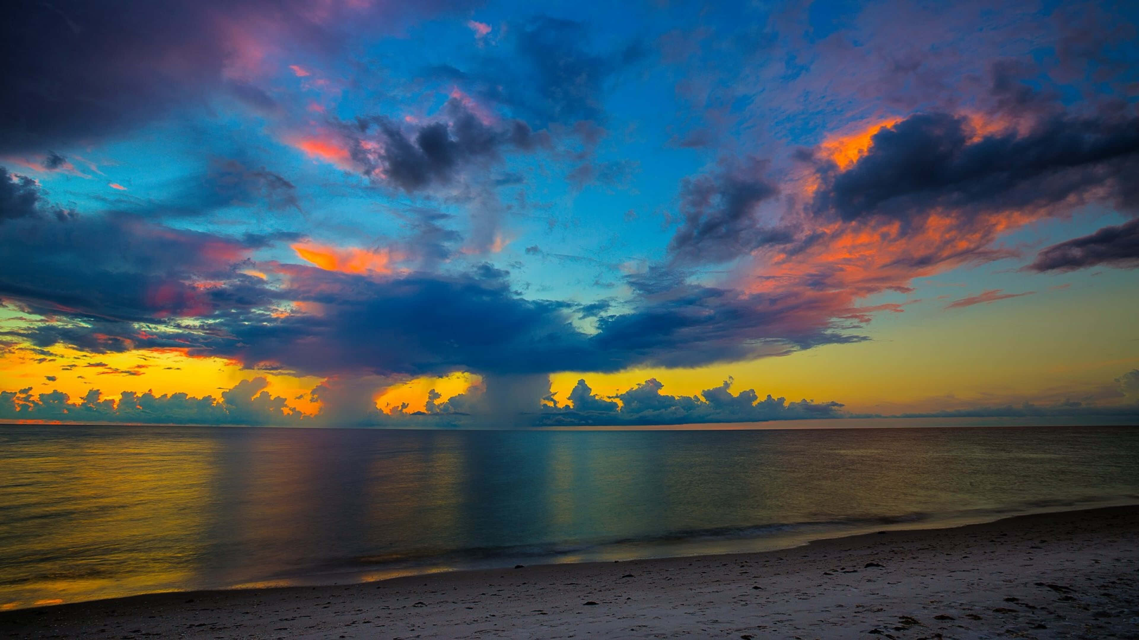 Colorful Sky 桌布 壁紙 — 平靜海洋上戲劇性的日落，火橙色和深藍色的雲彩倒映在水面上。