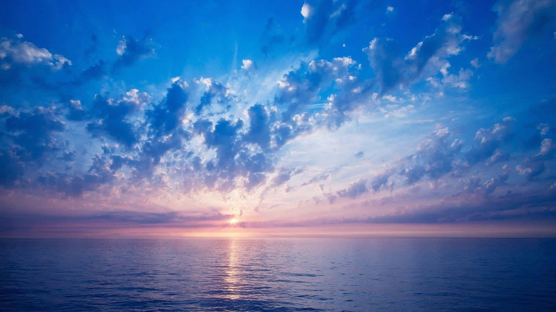 Beautiful Sky 桌布 壁紙 — 平靜海洋上的日落，鮮豔的藍色和紫色雲彩在水面上反射出金色光芒。