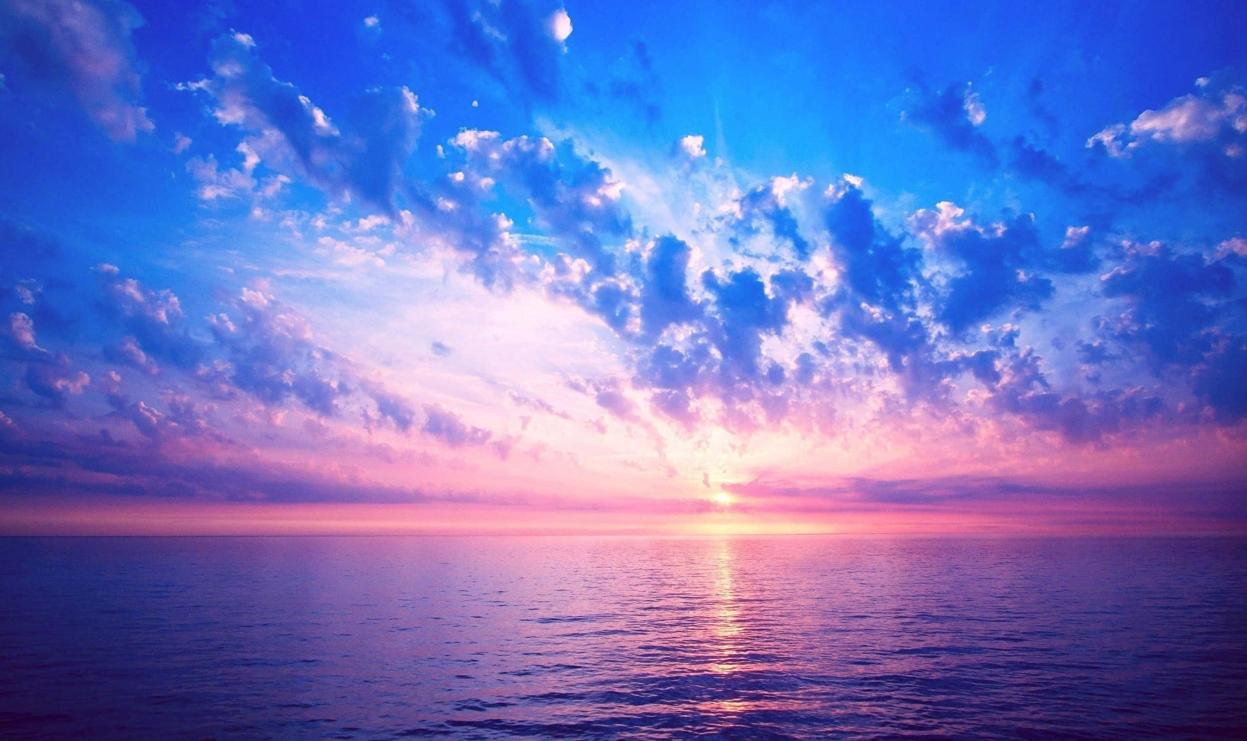Beautiful Sky 桌布 壁紙 — 平靜海面上充滿活力的日落，粉紅色和藍色的雲彩在水面上反射。