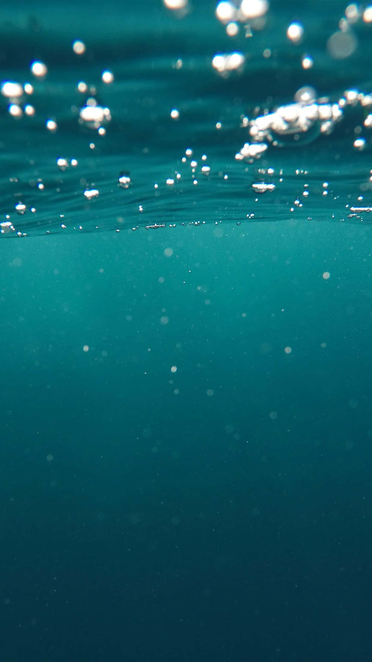 Underwater iPhone 桌布 壁紙 — 平靜的分割視圖，呈現碧綠色的海水，陽光照射的氣泡在表面升起，下方是寧靜的深處。