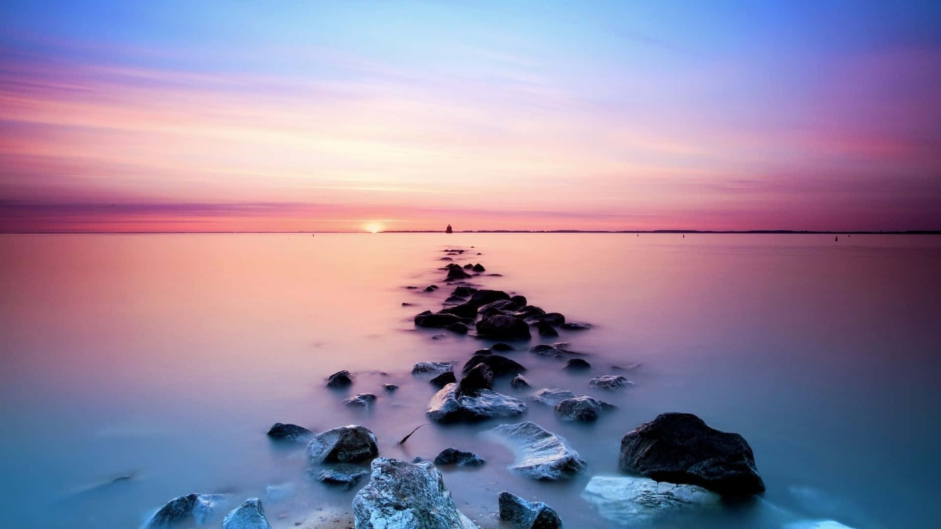 Calm Aesthetic 桌布 壁紙 — 平靜的水面上，夕陽西下，一條石徑在粉紅、紫和藍色的漸變天空下通往遠處的帆船，景色寧靜。