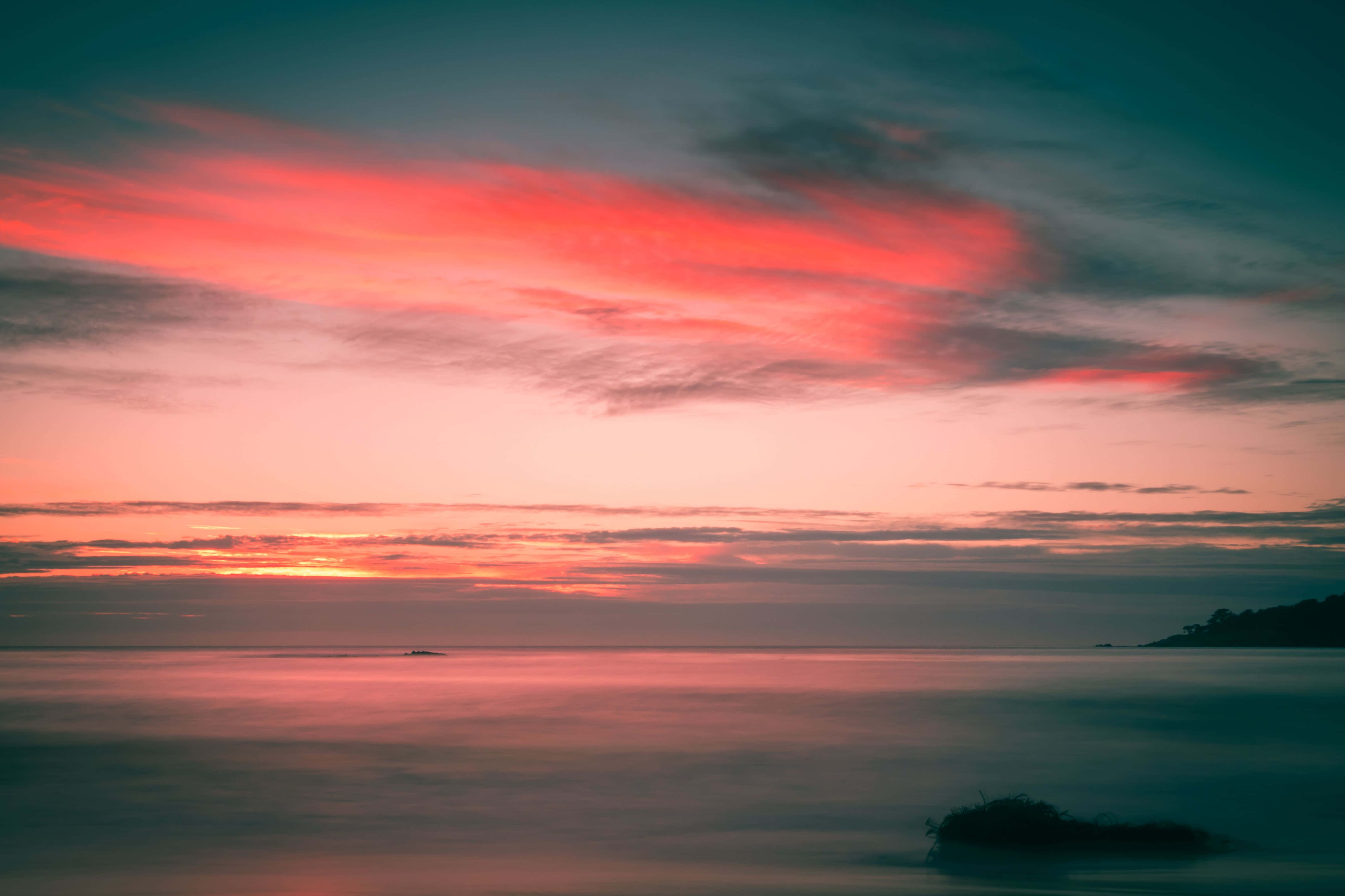 Pink Sunset 桌布 壁紙 — 平靜的水面上，夕陽西下，鮮豔的粉紅色和橙色雲彩倒映在玻璃般的水面上。