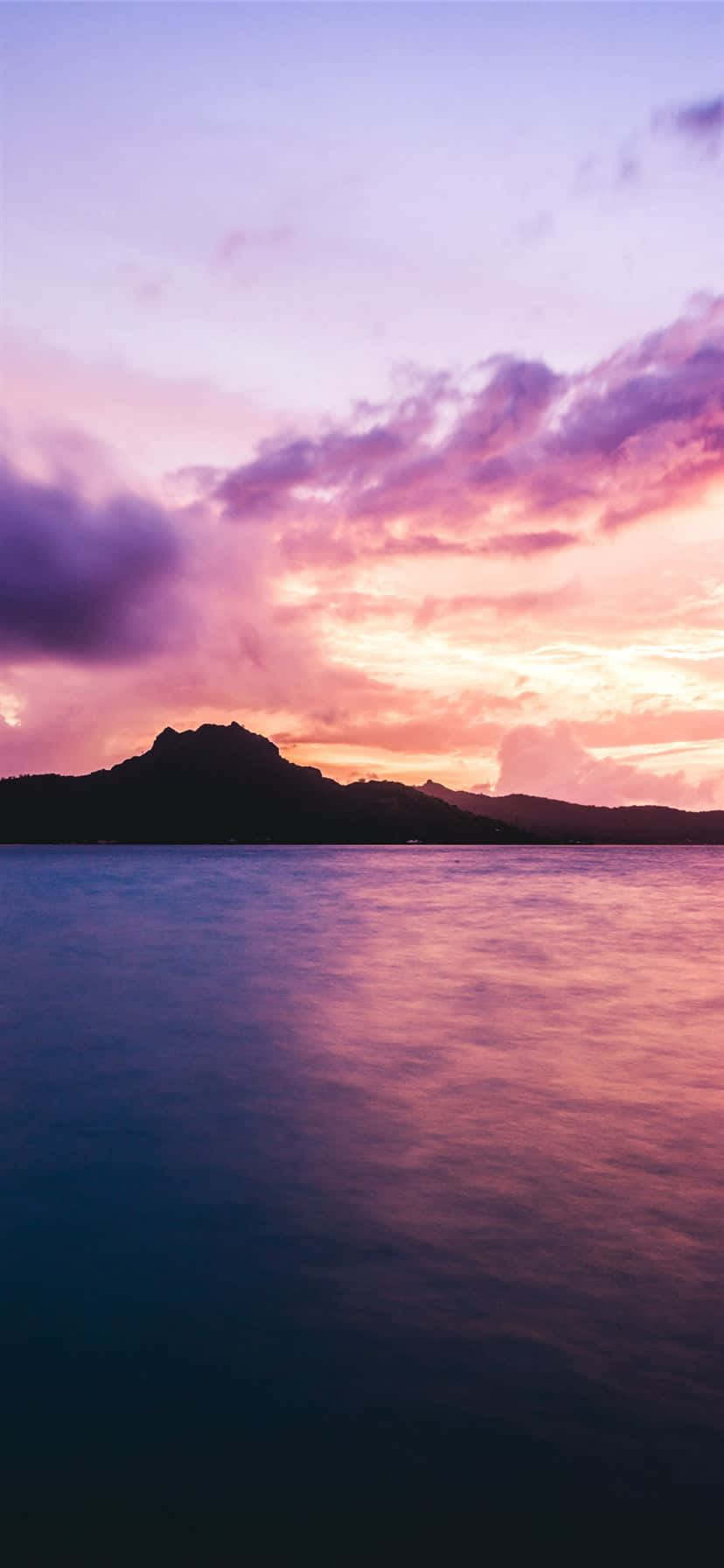 Bora Bora 桌布 壁紙 — 平靜的水面上寧靜的日落，黑暗的山脈輪廓在充滿活力的紫色和粉紅色天空下。
